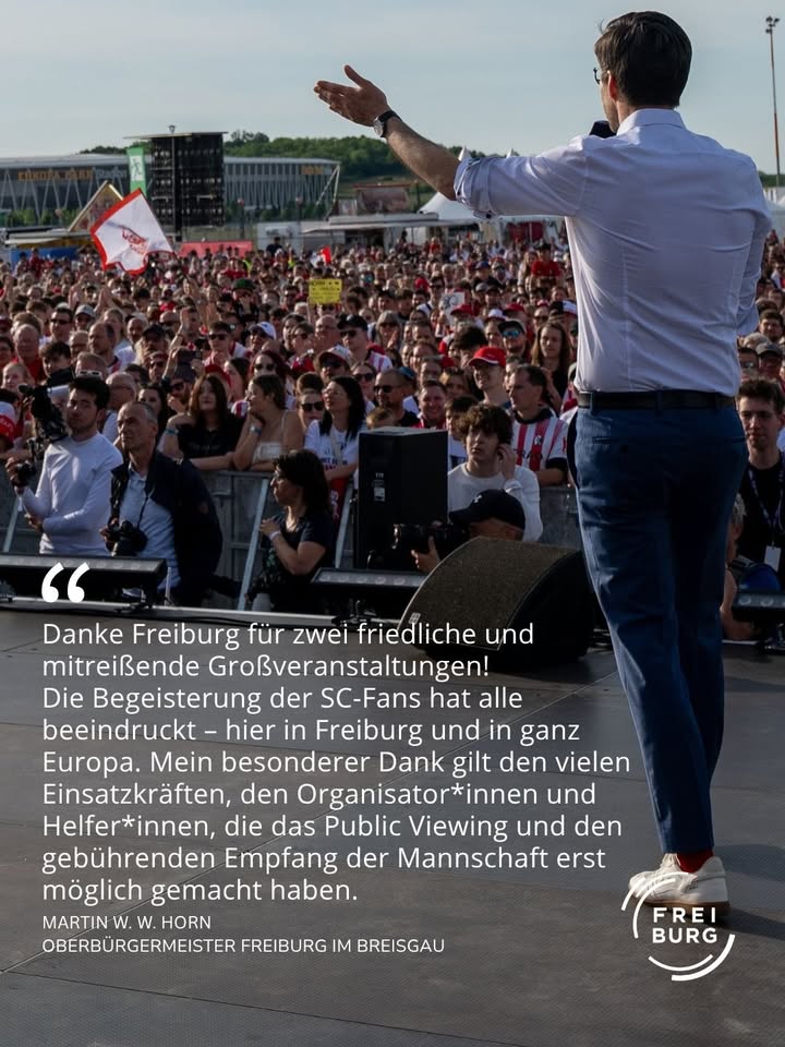 Eine Person steht auf einer Bühne vor einer großen Menschenmenge, gestikuliert mit erhobener Hand und spricht in ein Mikrofon. Im Vordergrund ist ein Textzitat zu lesen, das den SC-Fans und Helfer*innen für zwei friedliche Großveranstaltungen in Freiburg dankt, unterzeichnet von Martin W. W. Horn, Oberbürgermeister Freiburg im Breisgau. Rechts unten das Logo „Freiburg“. (KI-Alternativtext)