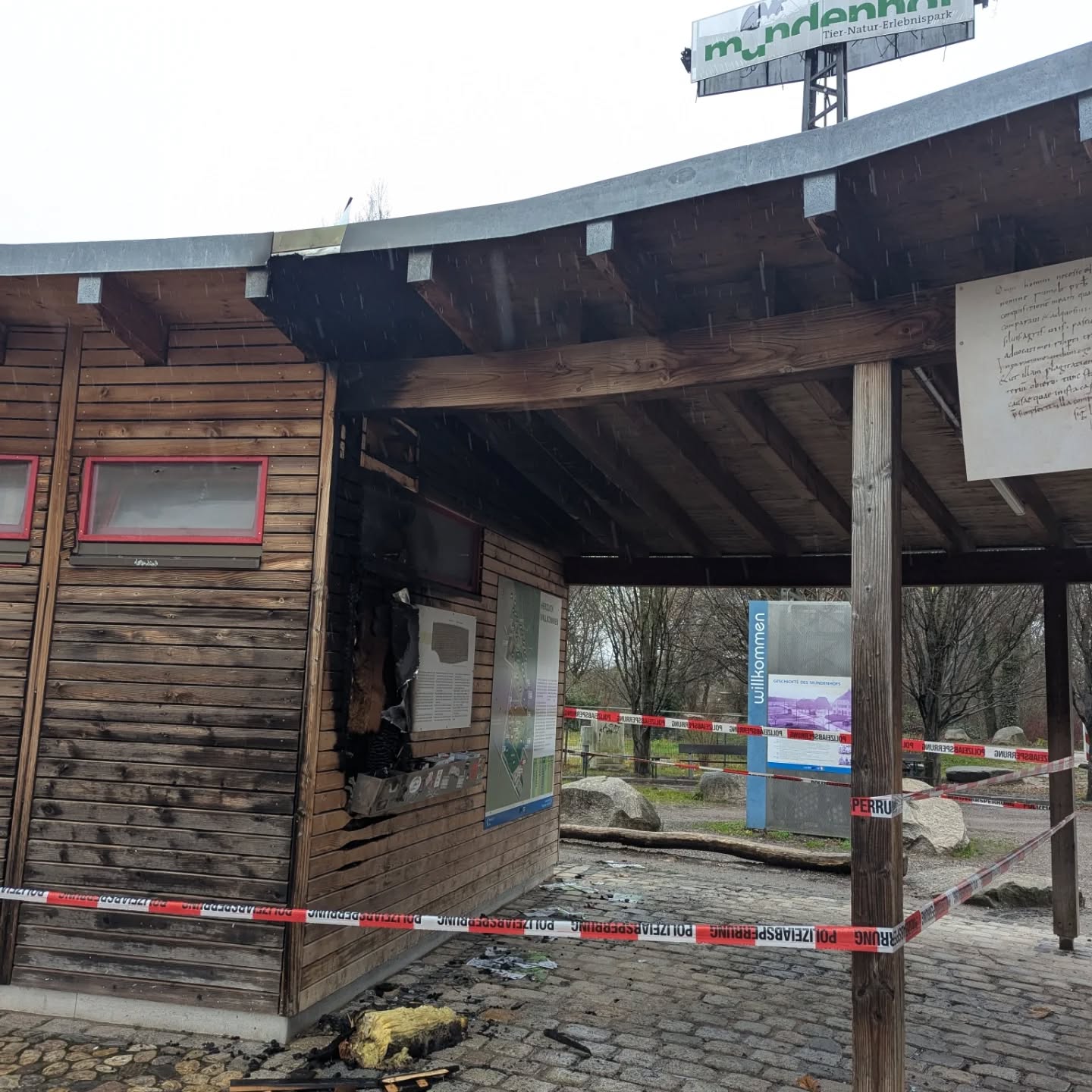 Dieser Alternativtext wurde KI-generiert: Ein hölzernes Gebäude steht vor einer unscharfen Hintergrundlandschaft. Das Gebäude ist teilweise mit Absperrbändern versehen.