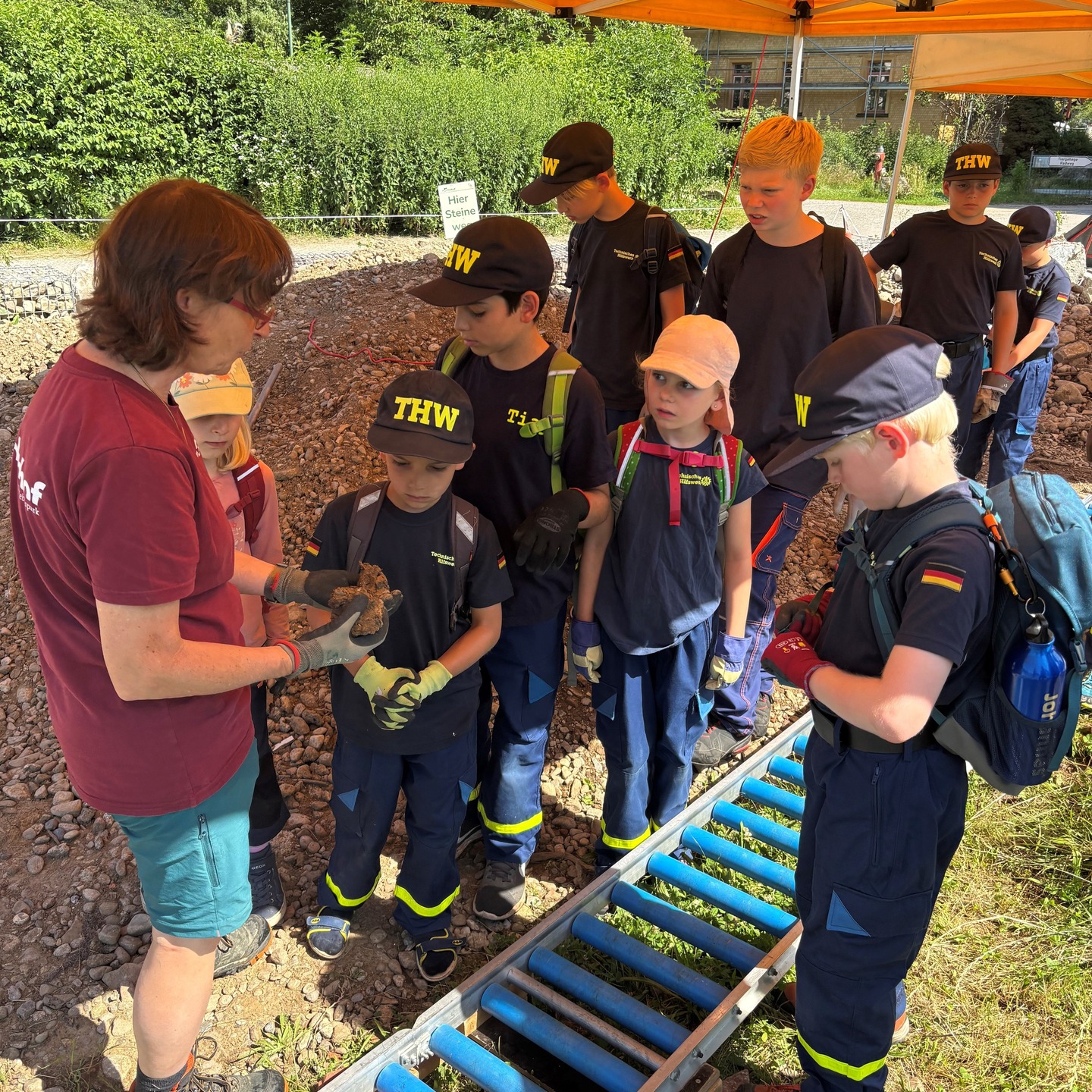 Mehrere Personen stehen im Freien. Eine Person hält einen Gegenstand in den Händen und zeigt ihn anderen Personen.