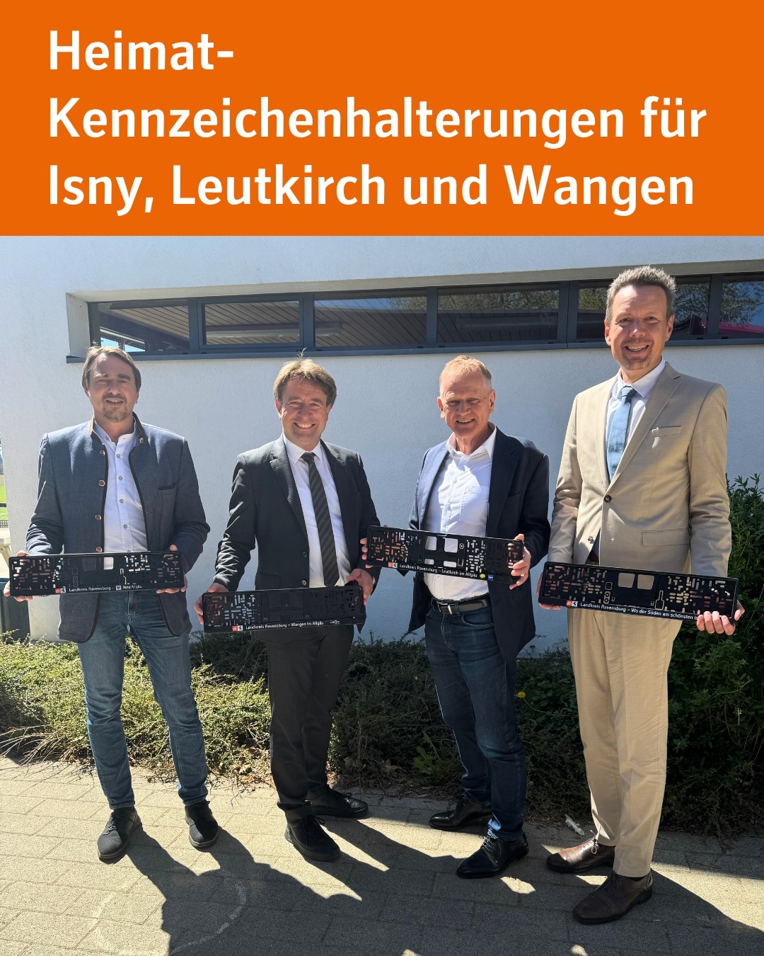 Auf dem Bild sind vier Männer zu sehen, welche jeweils eine Kennzeichenhalterung in die Kamera halten.

Bildtext: Heimat-Kennzeichenhalterungen für Isny, Leutkirch und Wangen