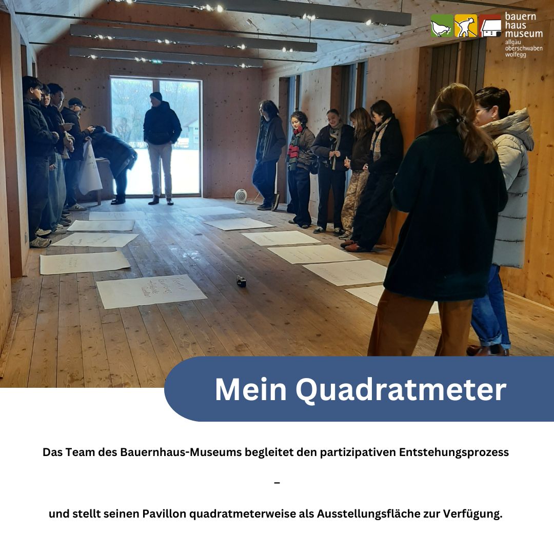 Dieser Alternativtext wurde KI-generiert: Eine Gruppe von Personen steht in einem hellen Raum mit Holzboden vor einer großen blauen Fläche mit Text. Das Bild ist farbig und zeigt ein Museumsprojekt zur partizipativen Gestaltung.