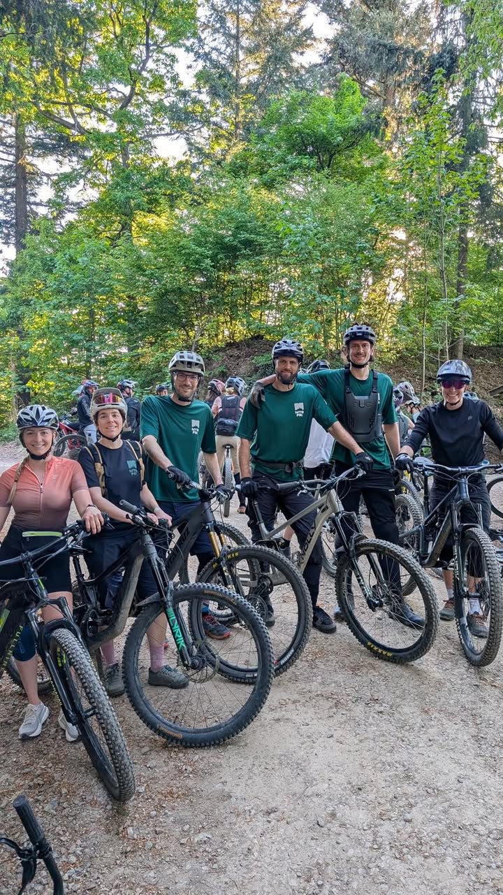 Dieser Alternativtext wurde KI-generiert: Eine Gruppe von Personen steht mit Fahrrädern auf einem Waldweg. Alle tragen Helme und grüne Oberteile.