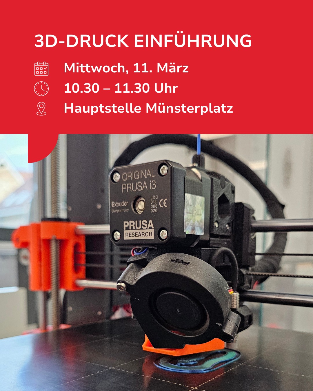 Dieser Alternativtext wurde KI-generiert: Ein Foto zeigt einen 3D-Drucker im Betrieb auf einer Arbeitsfläche. Im Hintergrund ist ein Veranstaltungsplakat mit Informationen zu einem 3D-Druck Einführungskurs zu sehen.