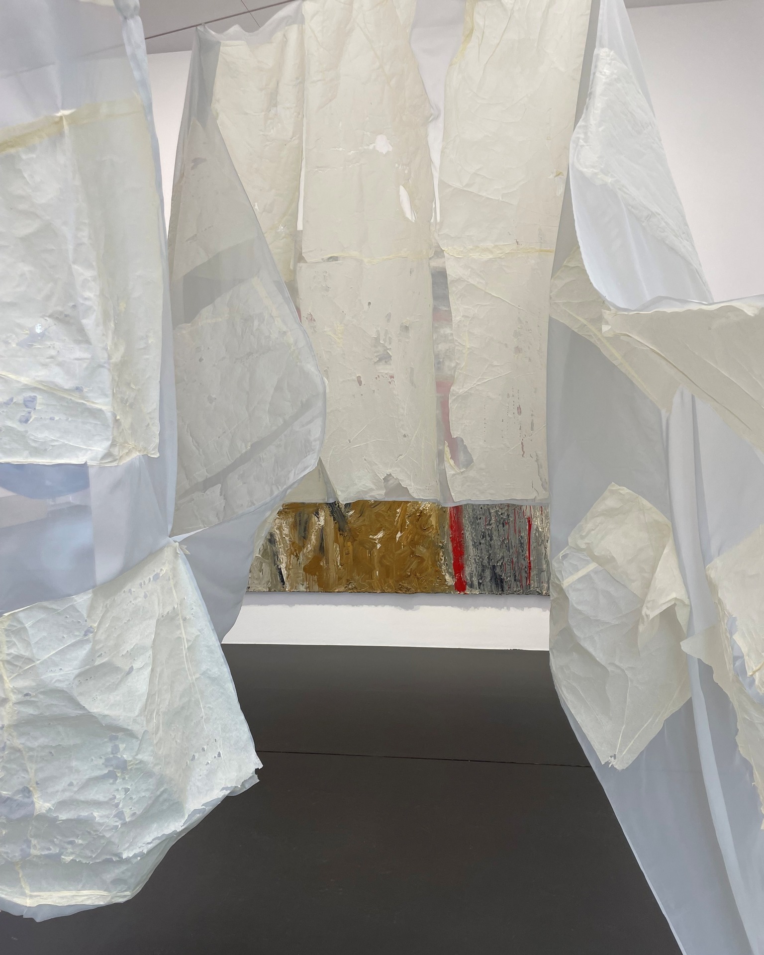 Dieser Alternativtext wurde KI-generiert: Abstrakte Kunstinstallation in Weiß und Gelb. Die Arbeit besteht aus verschiedenen Schichten und Formen, die vor einem farbigen Hintergrund hängen.