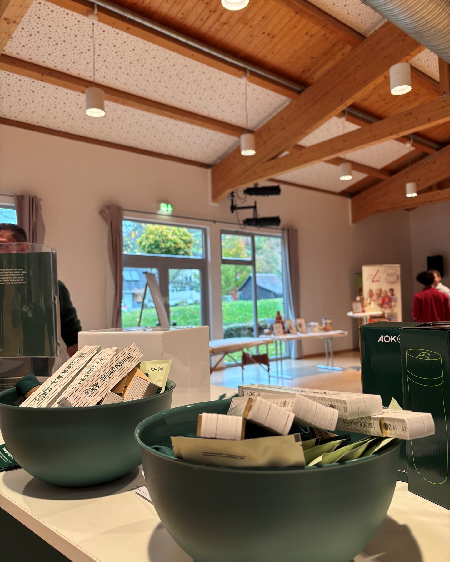 Dieser Alternativtext wurde KI-generiert: Ein Innenraum mit Holzbalken und großen Fenstern ist zu sehen. Im Vordergrund befindet sich eine dunkle Schale mit Rollen, vermutlich von einer Veranstaltung.
