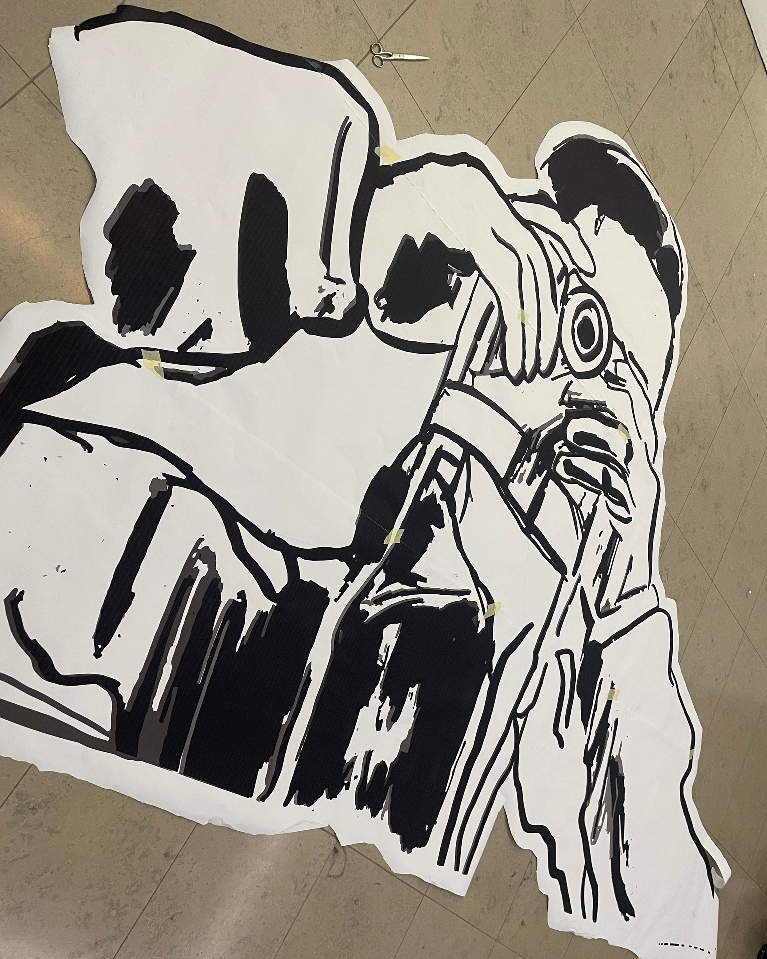 Dieser Alternativtext wurde KI-generiert: Schwarz-Weiß-Foto einer Person, die mit einer Schere an einem großen Papierobjekt arbeitet. Es scheint sich um eine Kreation aus ausgeschnittenen und angeklebten Formen zu handeln.