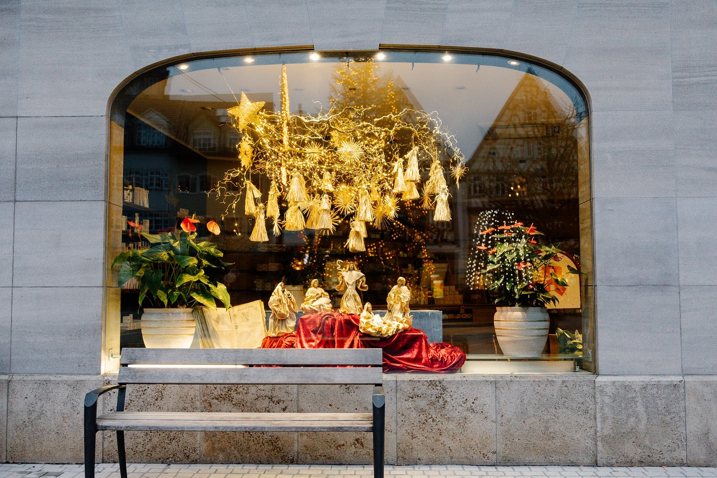 Ein Schaufenster mit einer Weihnachtskrippe und goldener Dekoration. Vor dem Schaufenster steht eine Bank.