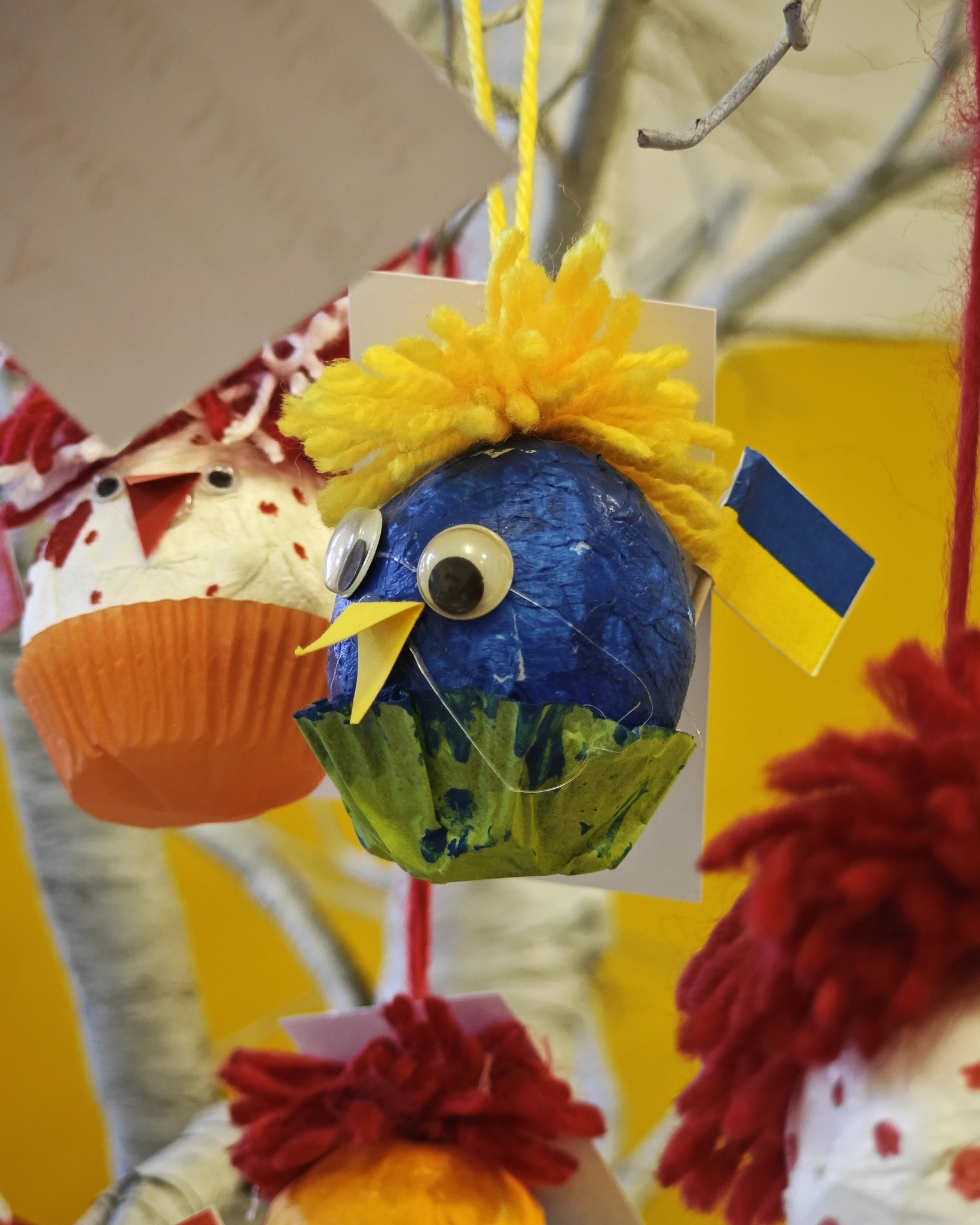 Dieser Alternativtext wurde KI-generiert: Eine Nahaufnahme von handgefertigten, bunten Dekorationen, die an Ästen hängen. Die Dekorationen bestehen aus verschiedenen Materialien und haben tierähnliche Formen.