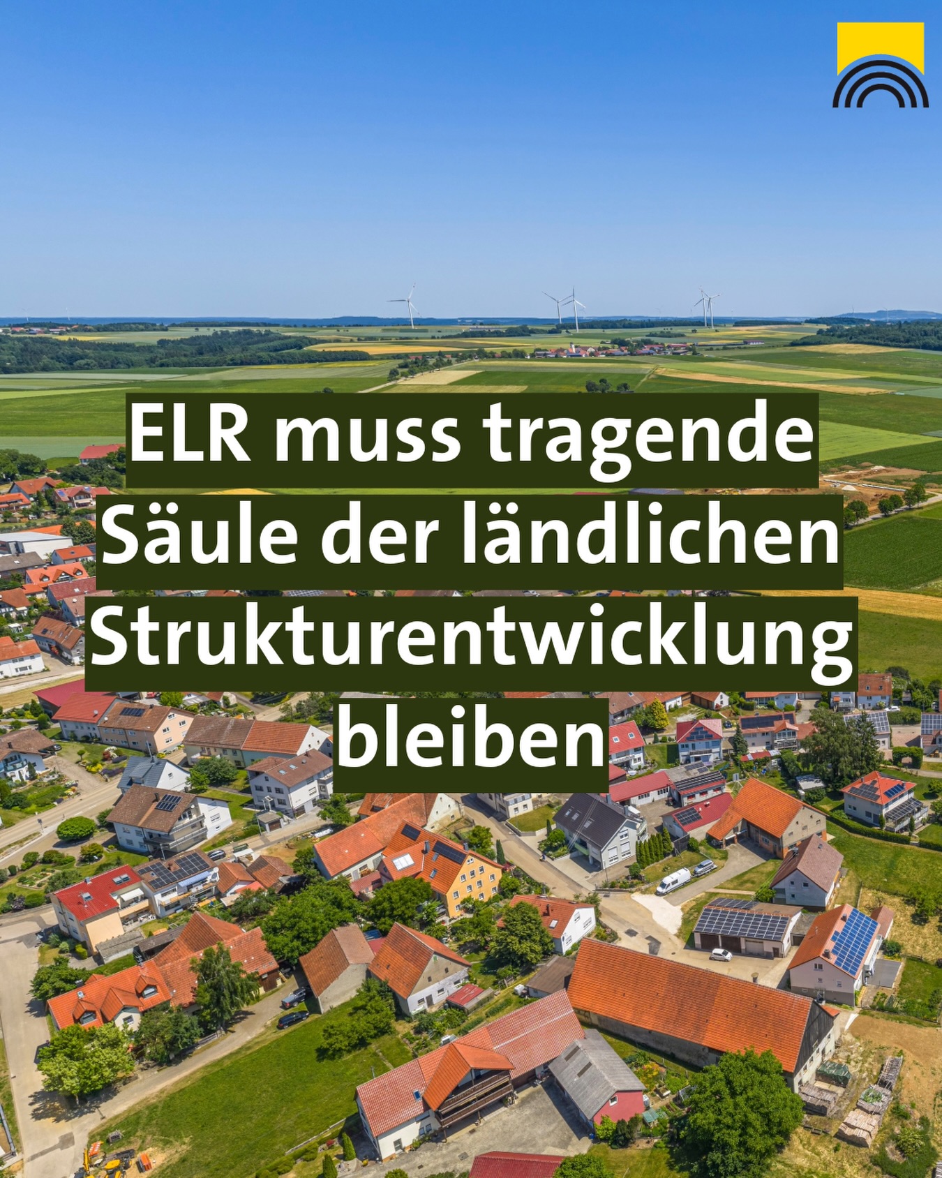 Dieser Alternativtext wurde KI-generiert: Eine Aufnahme von einem Dorf oder einer Stadt aus der Vogelperspektive, umgeben von Feldern und Windrädern. Im Vordergrund befindet sich ein Textfeld mit weißer Schrift auf dunklem Hintergrund.