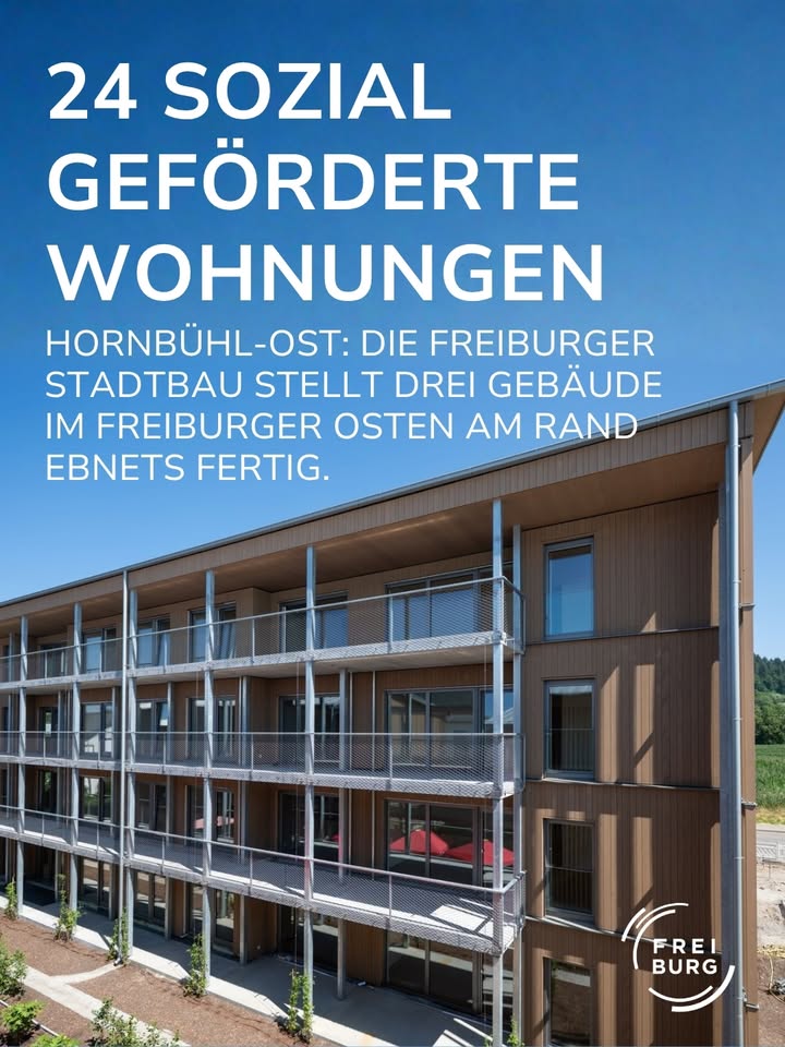 „24 SOZIAL GEFÖRDERTE WOHNUNGEN“ ist die große weiße Überschrift. Darunter steht: „HORNBÜHL-OST: DIE FREIBURGER STADTBAU STELLT DREI GEBÄUDE IM FREIBURGER OSTEN AM RAND EBNETS FERTIG.“ Das Bild zeigt ein modernes Mehrfamilienhaus mit brauner Holzfassade und Balkonen vor blauem Himmel. Unten rechts befindet sich das Logo „FREIBURG“. (KI-Alternativtext)