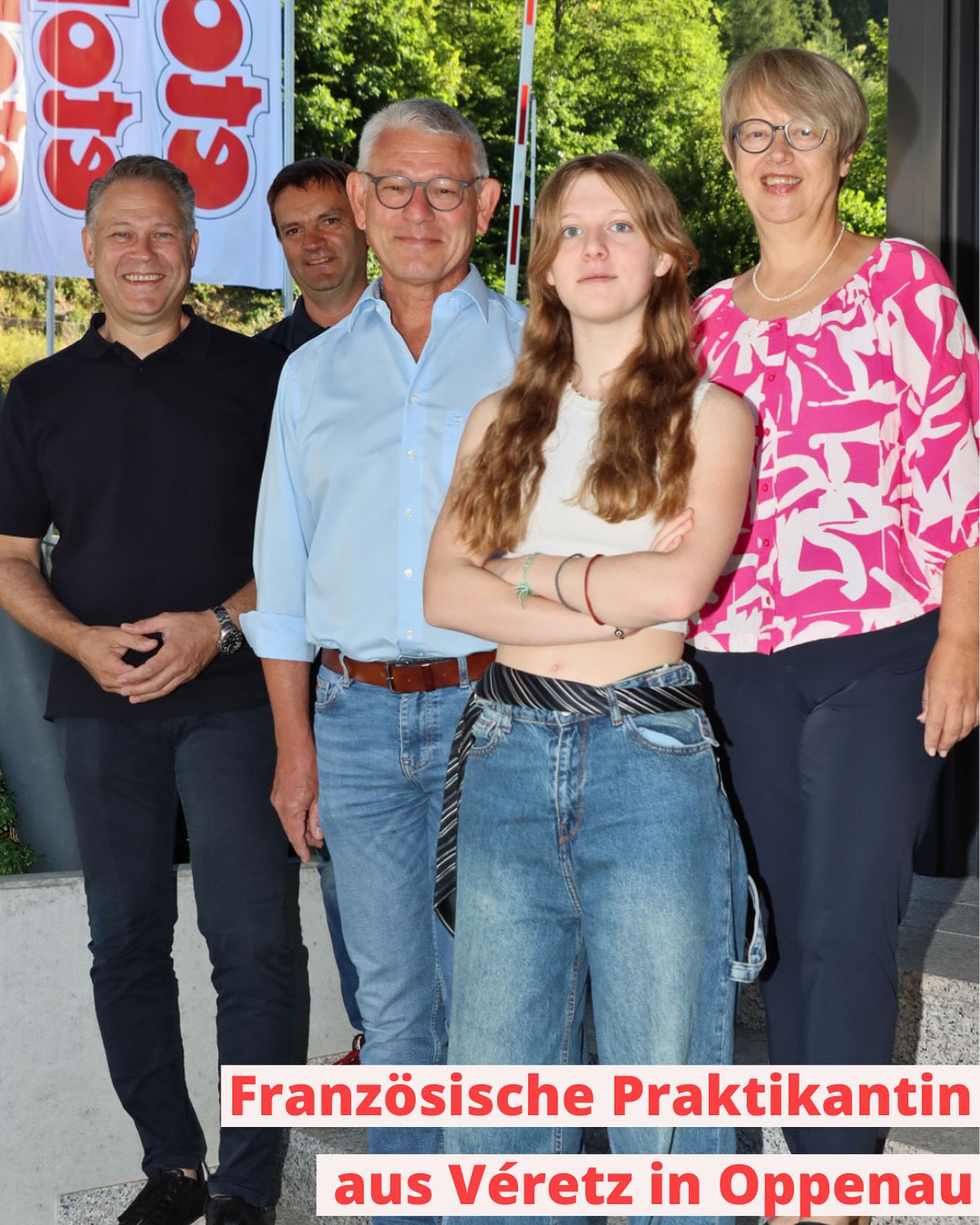 Eine Gruppe von fünf Personen steht im Freien. Im Hintergrund ist ein teilweise sichtbares Transparent zu sehen.