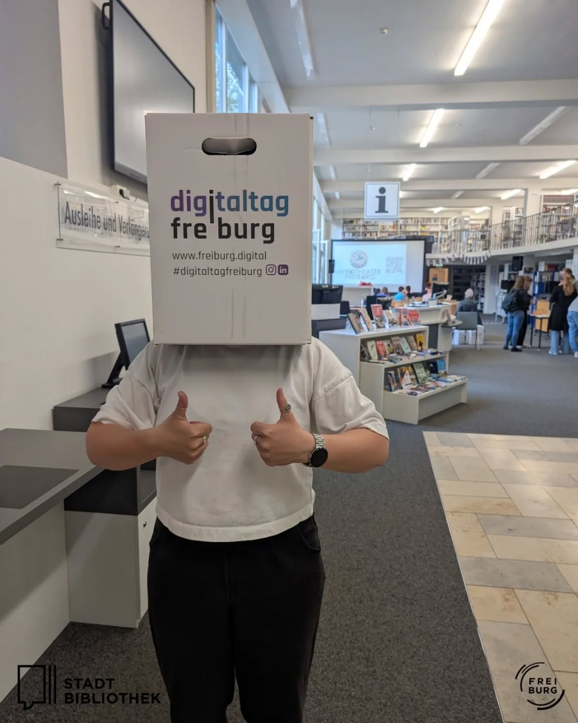 Dieser Alternativtext wurde KI-generiert: Eine Person hält eine Schachtel mit Text vor dem Gesicht. Im Hintergrund ist ein Bibliotheksraum mit Bücherregalen zu sehen.
