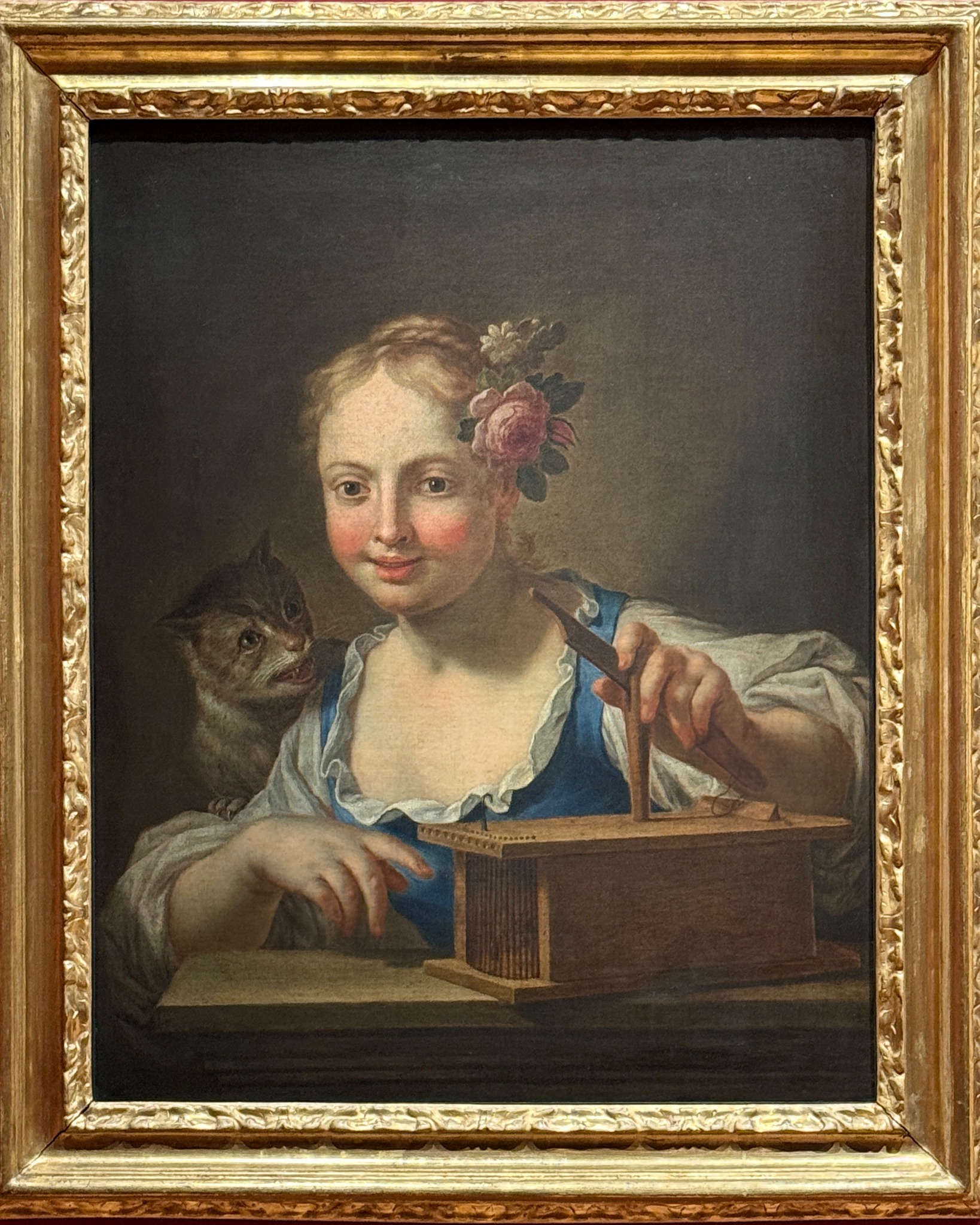 Eine Person mit einer Blume im Haar spielt ein hölzernes Saiteninstrument, während eine Katze auf der Schulter sitzt. Das Gemälde ist in einem goldenen Rahmen. (KI-Alternativtext)