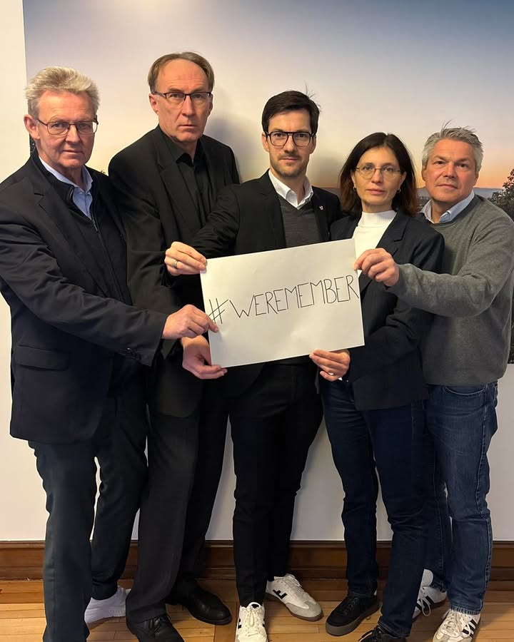 Dieser Alternativtext wurde KI-generiert: Fünf Personen stehen zusammen und halten ein Schild mit einem Hashtag hoch. Das Bild ist farbig und zeigt die Gruppe in formeller und legerer Kleidung.