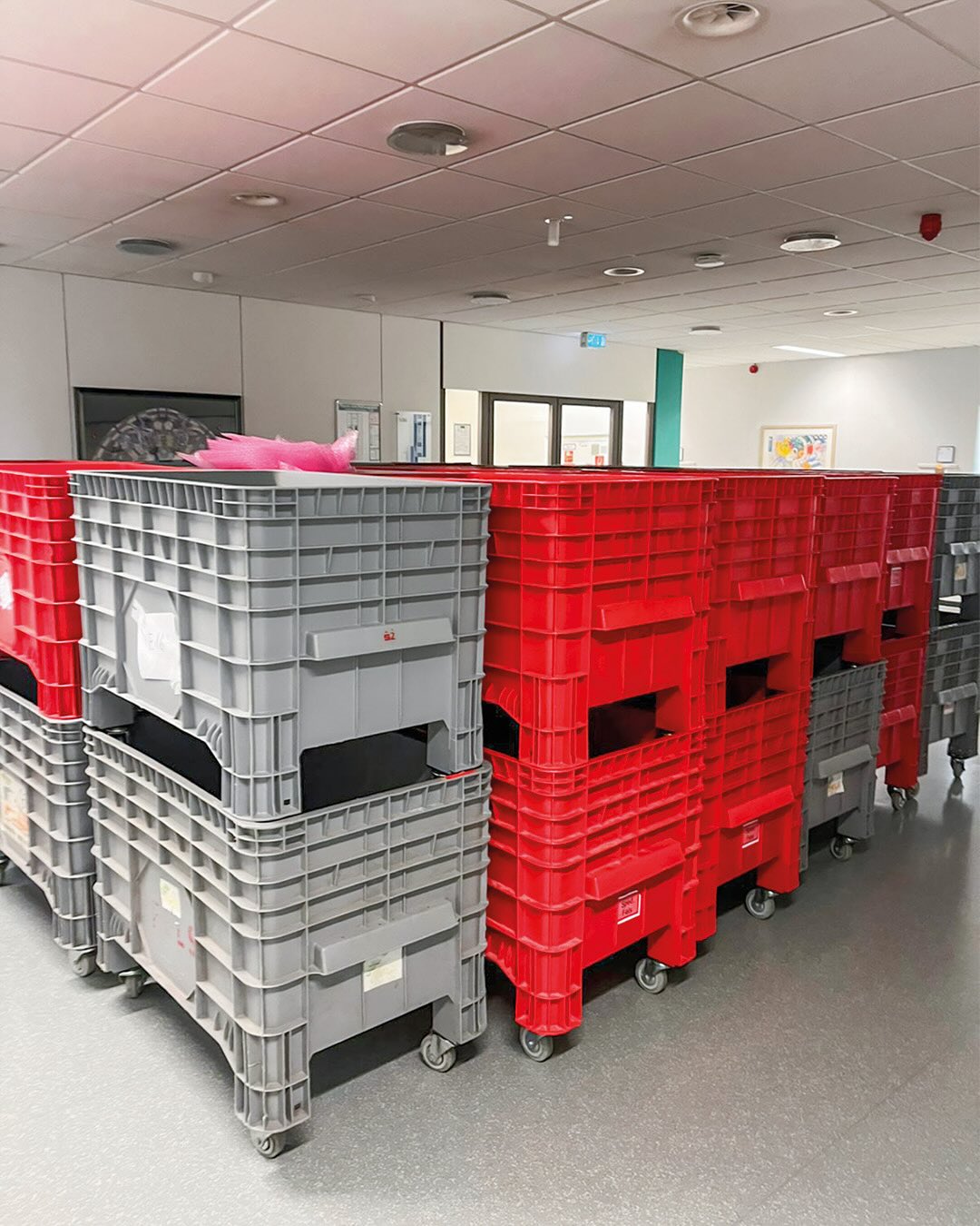 Dieser Alternativtext wurde KI-generiert: Mehrere gestapelte, farbige Kisten auf Rollen stehen in einem hellen Raum. Im Hintergrund sind Türen und ein Fenster zu sehen.
