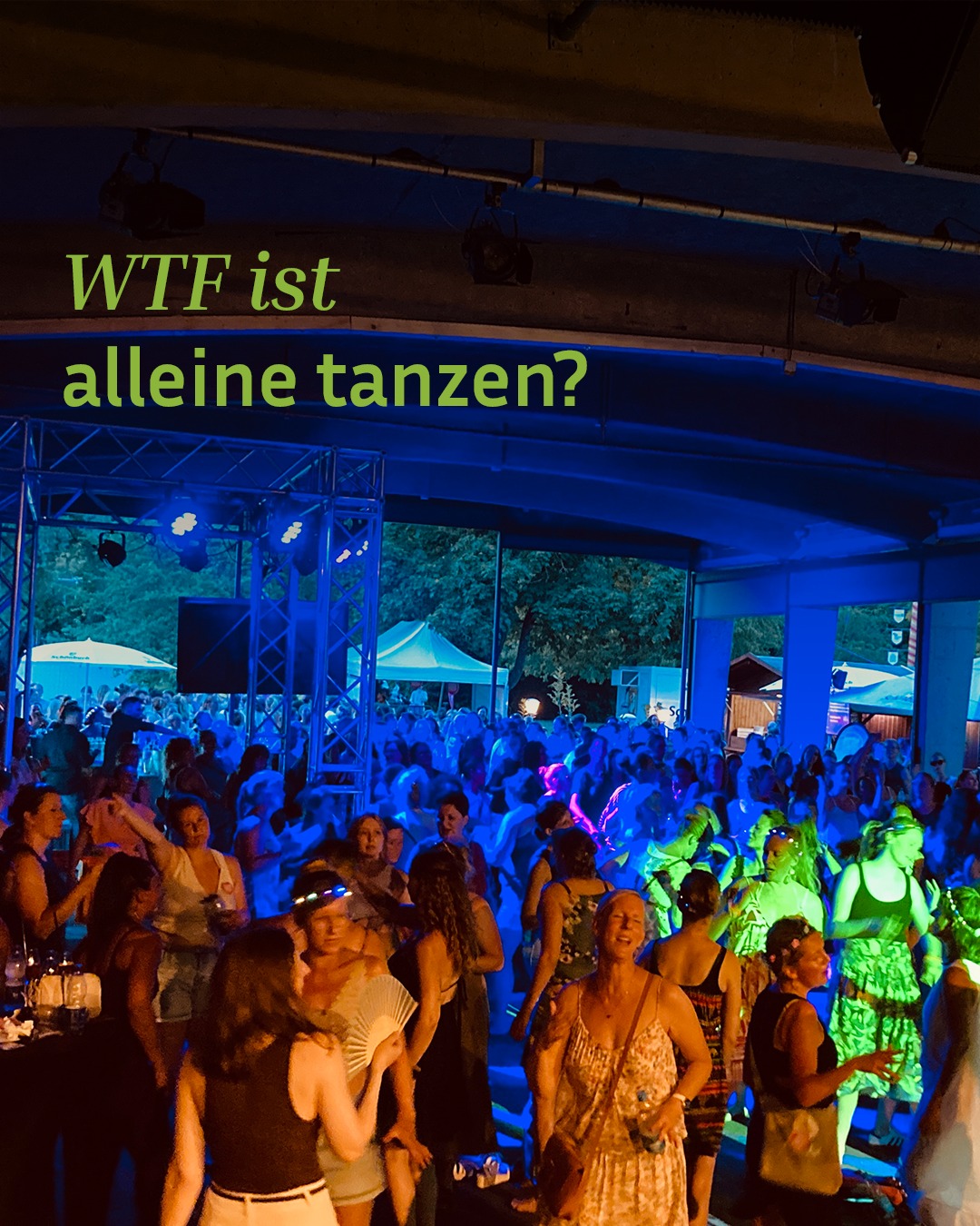 Auf einer belebten Tanzfläche unter blauem und grünem Licht tanzen viele Personen. Oben links ist der grüne Text "WTF ist alleine tanzen?" eingeblendet. Im Vordergrund sind mehrere tanzende Personen zu sehen, die sich allein oder in kleinen Gruppen bewegen. (KI-Alternativtext)