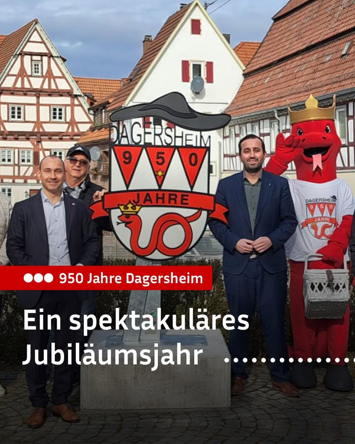 Dieser Alternativtext wurde KI-generiert: Eine Aufnahme von mehreren Personen vor Fachwerkhäusern. Im Vordergrund befindet sich ein Schild mit einer Zahl und einem Wappen.