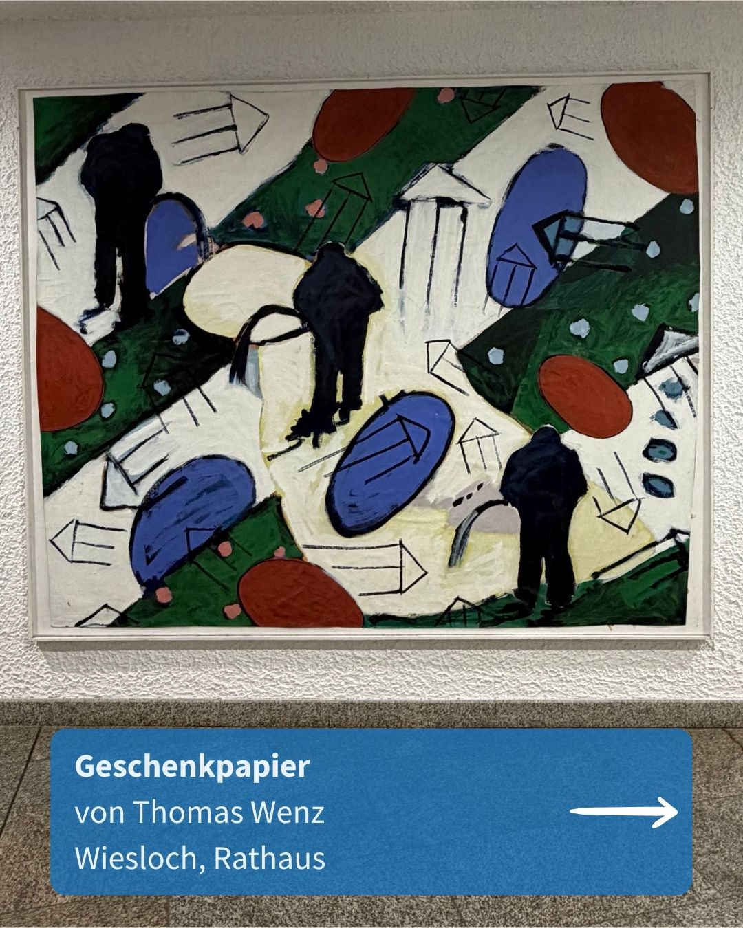 Ein gerahmtes Gemälde zeigt drei schwarze Personen-Silhouetten in einer abstrakten Landschaft mit grünen Flächen, blauen und roten Ovalen sowie skizzenhaften Häusern. Darunter hängt ein blaues Schild mit der weißen Aufschrift „Geschenkpapier von Thomas Wenz Wiesloch, Rathaus“ und einem nach rechts zeigenden Pfeil. (KI-Alternativtext)