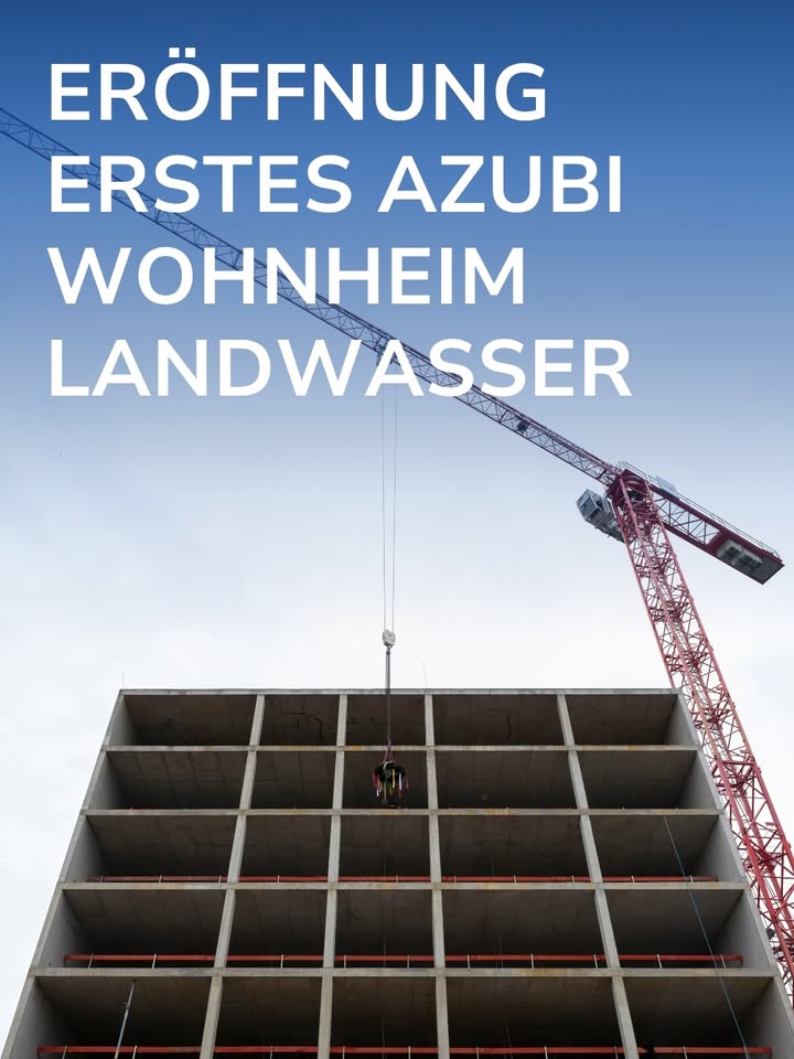Ein mehrstöckiges Betonbauwerk im Rohbau steht im Vordergrund, während ein roter Turmdrehkran diagonal in den Himmel ragt. Über dem Bild steht in weißen Großbuchstaben der Text: ERÖFFNUNG ERSTES AZUBI WOHNHEIM LANDWASSER. (KI-Alternativtext)