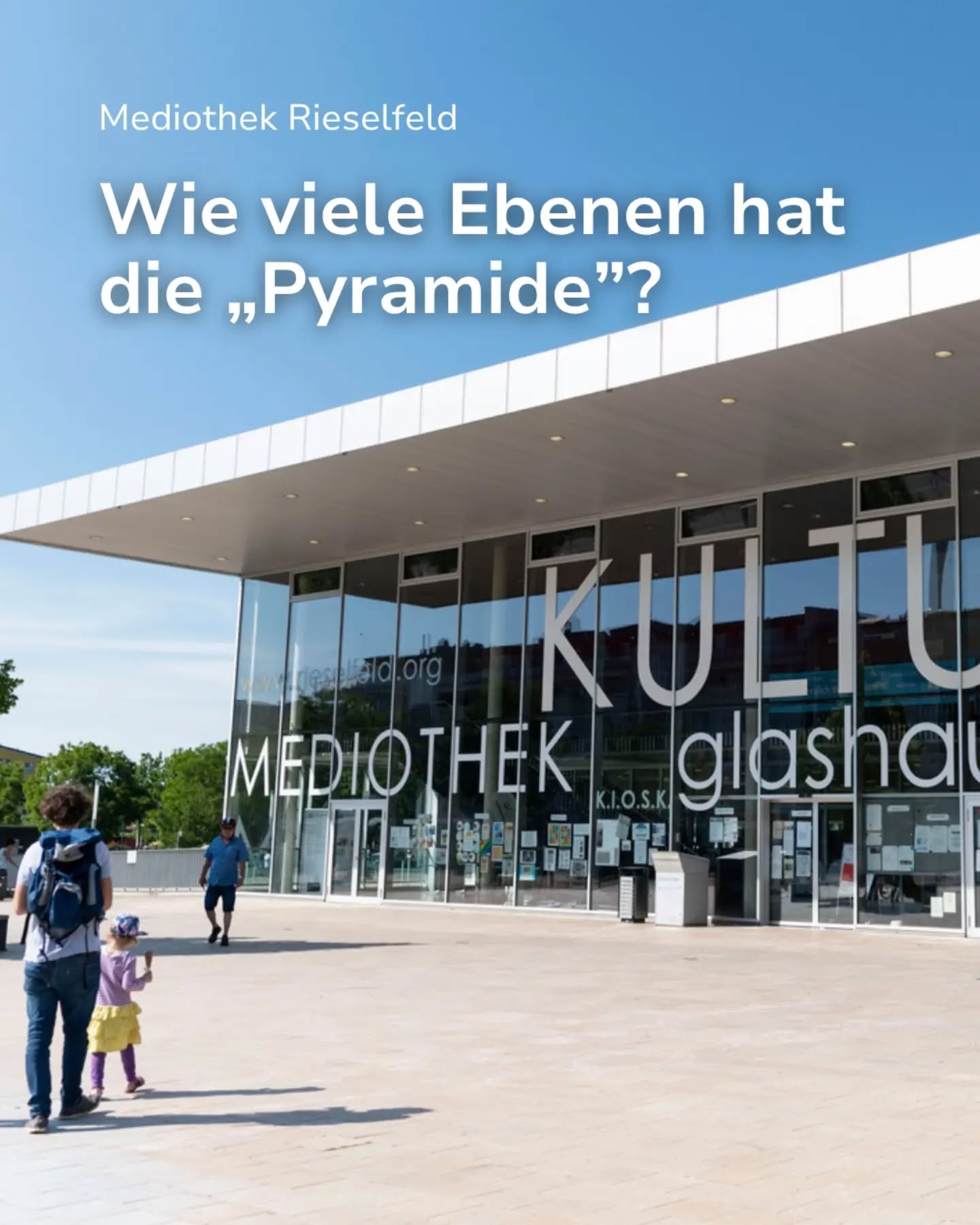 Der Text "Mediothek Rieselfeld" und die Frage "Wie viele Ebenen hat die „Pyramide“?" sind oben im Bild eingeblendet. Im Hintergrund steht ein modernes Glasgebäude mit den Aufschriften "KULTUR glashaus" und "MEDIOTHEK". Im Vordergrund gehen eine Person mit Rucksack und ein Kind auf dem Pflasterweg. (KI-Alternativtext)