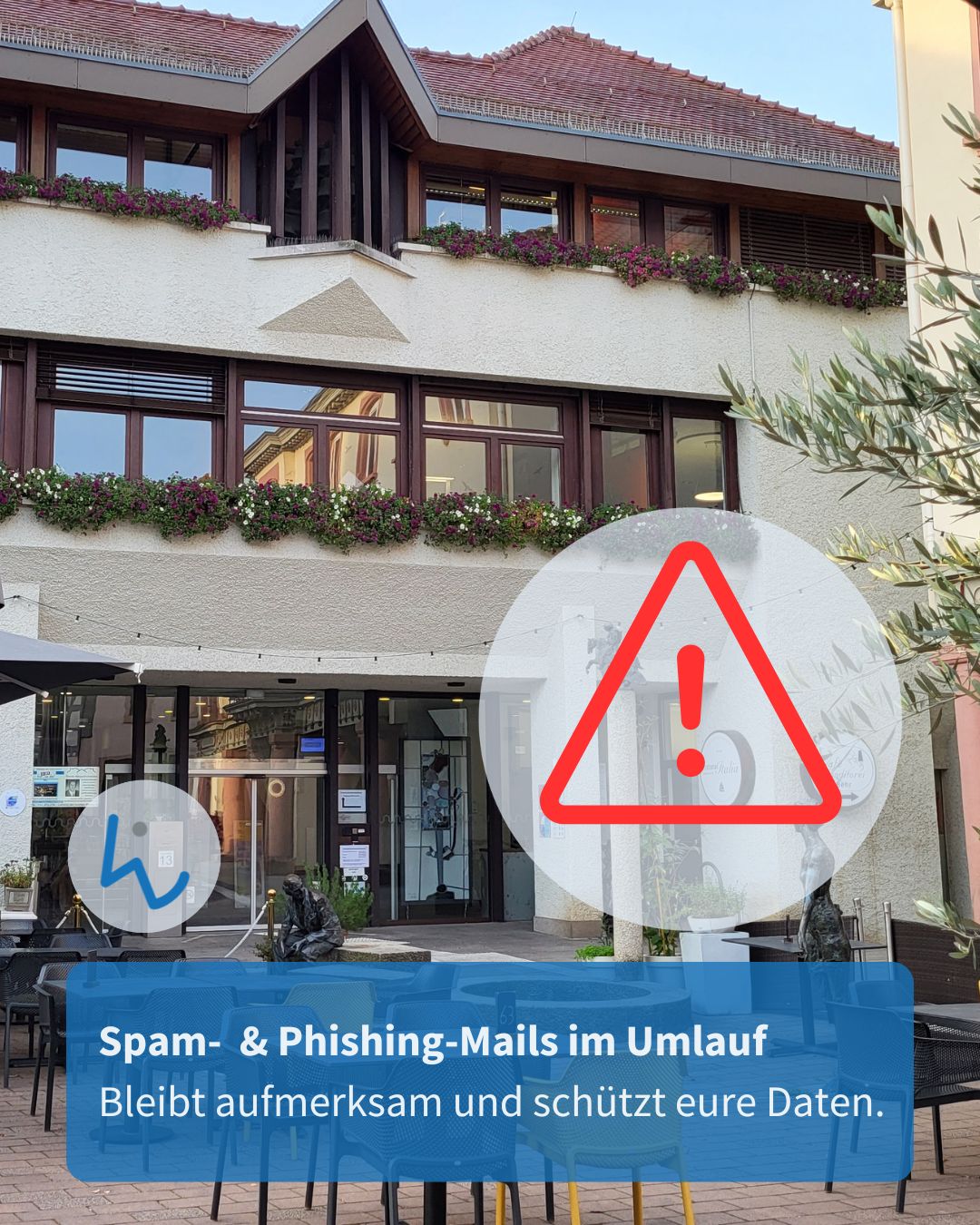 Dieser Alternativtext wurde KI-generiert: Ein Gebäude mit Blumenkästen und einer Warnung vor Spam- und Phishing-Mails im Vordergrund. Ein Warnschild mit einem Ausrufezeichen ist deutlich sichtbar.