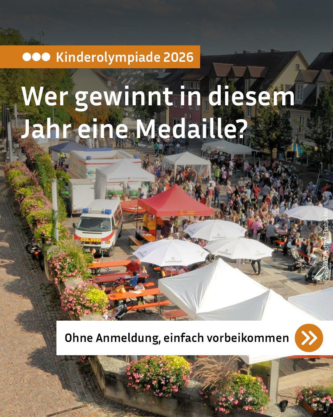 Ein Platz ist mit vielen Menschen, weißen und roten Zelten sowie weißen Sonnenschirmen gefüllt. Ein Rettungswagen steht neben orangefarbenen Tischen und blühenden Blumenbeeten an einer Mauer. Der Text "Kinderolympiade 2026 – Wer gewinnt in diesem Jahr eine Medaille? Ohne Anmeldung, einfach vorbeikommen" ist eingeblendet. (KI-Alternativtext)
