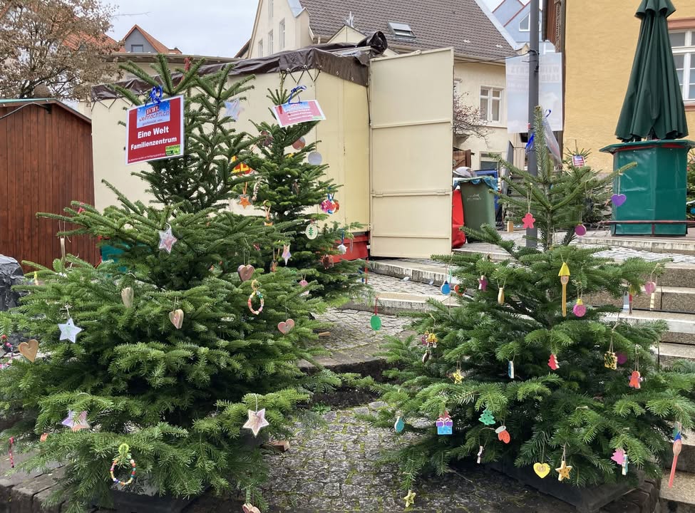 Dieser Alternativtext wurde KI-generiert: Mehrere mit Ornamenten geschmückte Weihnachtsbäume stehen vor einer Gebäudefront. Die Bäume sind mit verschiedenen Dekorationen wie Herzen und Sternen verziert.