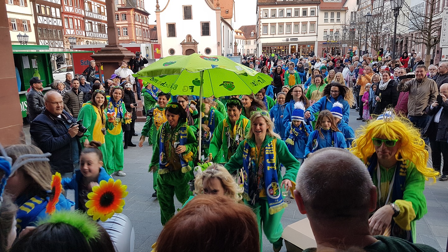 Eine Gruppe von Menschen in bunten Kostümen und Masken nimmt an einer Straßenparade teil. Sie tragen bunte Kleidung und Accessoires.