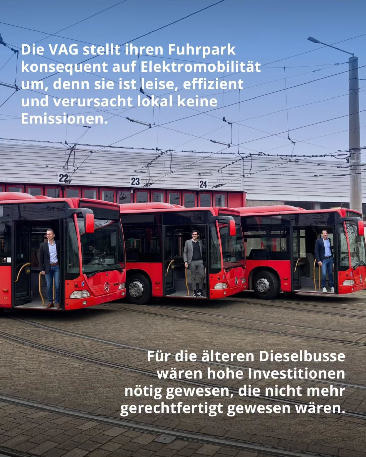 Dieser Alternativtext wurde KI-generiert: Mehrere rote Busse stehen auf Gleisen nebeneinander. Menschen stehen vor den Bussen und schauen zur Kamera.