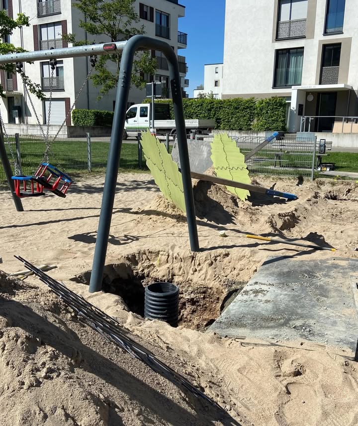 Dieser Alternativtext wurde KI-generiert: Ein Spielplatz mit einer Schaukel und einem Baugerüst im Vordergrund. Im Hintergrund sind Gebäude und Bäume bei Tageslicht zu sehen.