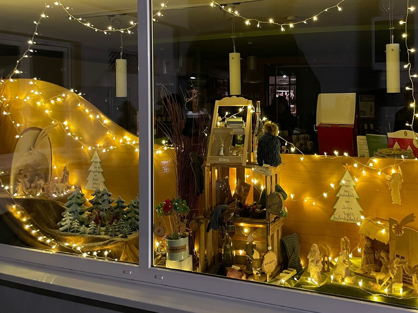 Festlich geschmücktes Schaufenster mit Krippenszene und weihnachtlichen Dekorationen. Warme, goldene Lichter erzeugen eine gemütliche Stimmung.