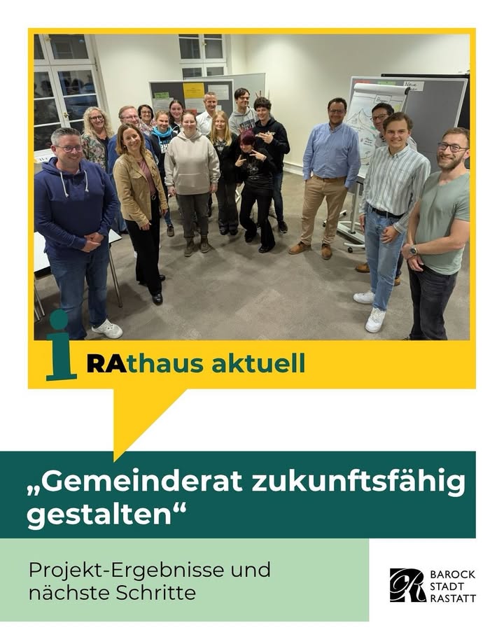 Dieser Alternativtext wurde KI-generiert: Eine Gruppe von Personen steht in einem Innenraum vor einem Fenster. Unter der Gruppe befindet sich ein Banner mit Text und einem Logo.