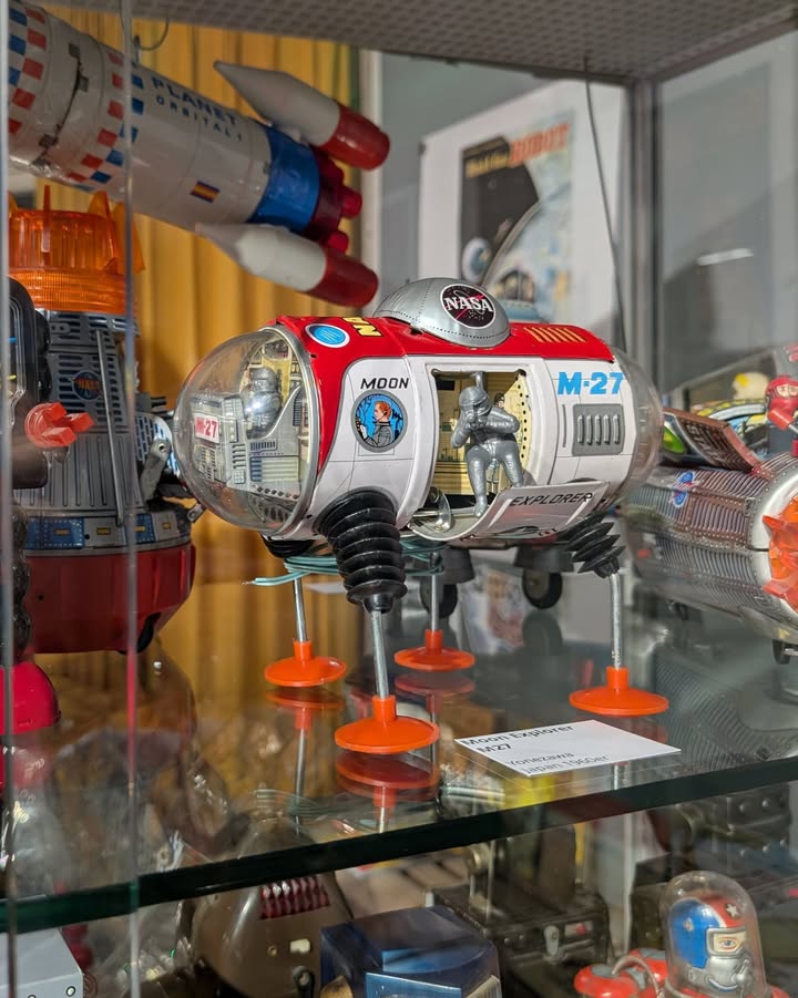 Dieser Alternativtext wurde KI-generiert: Eine Sammlung von Weltraumfahrzeug-Spielzeugmodellen steht hinter Glas ausgestellt. Die Modelle sind in verschiedenen Farben und Formen gestaltet und weisen Details wie NASA-Logos und Beschriftungen auf.