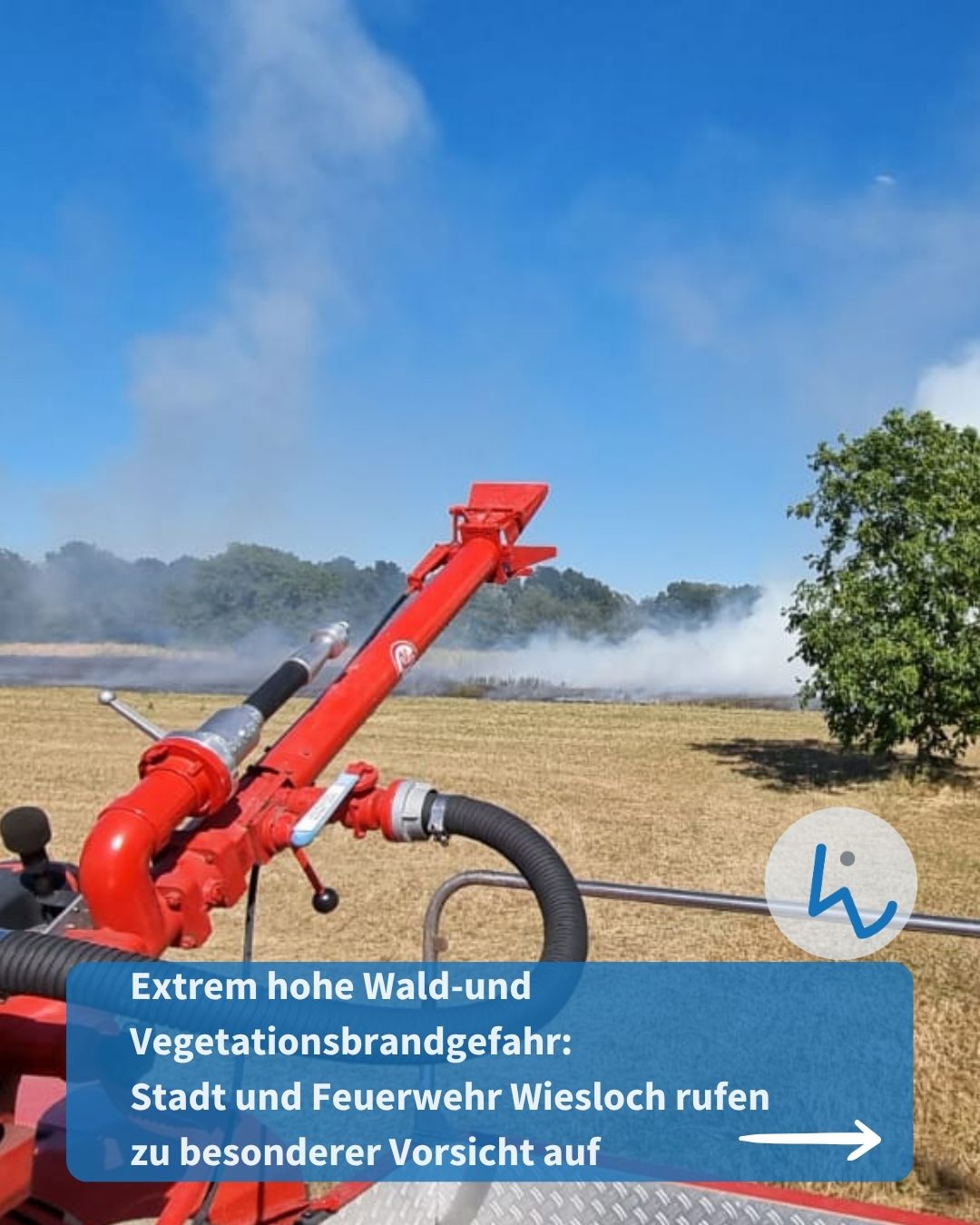 Roter Feuerlöschmonitor im Vordergrund auf einem trockenen Feld, im Hintergrund steigt Rauch über der Baumlinie auf. Ein blauer Textbalken unten lautet: „Extrem hohe Wald-und Vegetationsbrandgefahr: Stadt und Feuerwehr Wiesloch rufen zu besonderer Vorsicht auf“. (KI-Alternativtext)