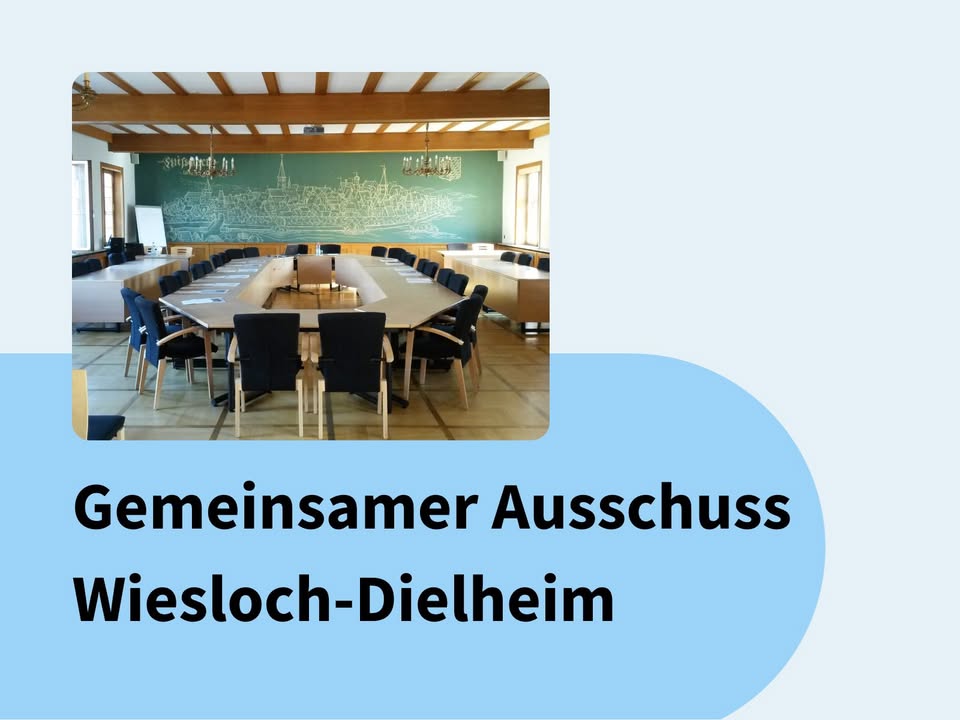 Dieser Alternativtext wurde KI-generiert: Ein heller Raum mit einem großen Konferenztisch und Stühlen. An einer Wand hängt eine große, dunkle Darstellung einer Stadtansicht.