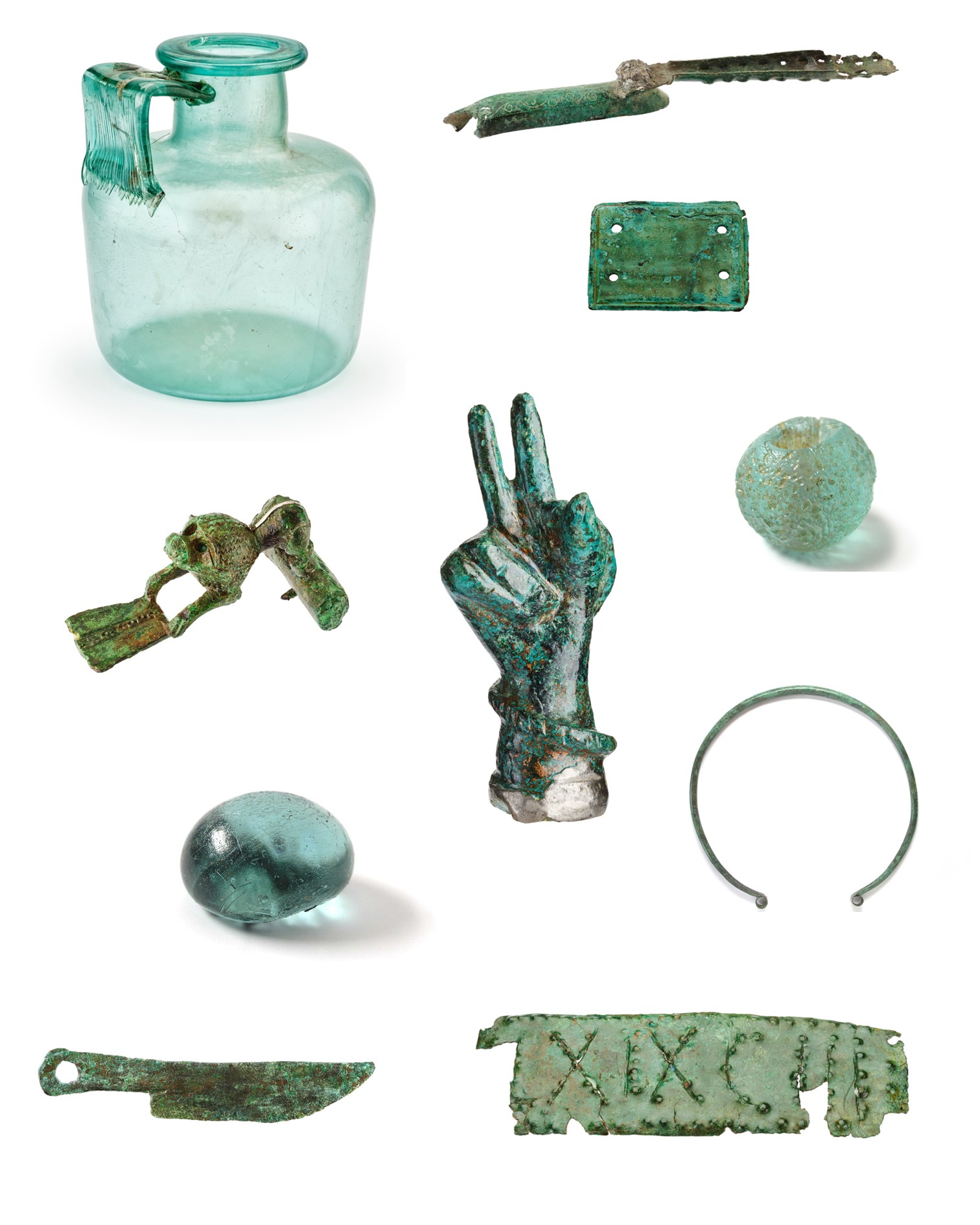 Sammlung antiker Objekte auf weißem Hintergrund, darunter eine hellblaue Glasflasche mit Henkel, zwei gläserne Kugeln, ein Metallring und diverse korrodierte Metallteile. Dazu zählen ein Messer, ein Griff, eine Hand, die zwei Finger erhebt, eine kleine Figur, eine Platte mit vier Löchern und ein Streifen mit römischen Ziffern. (KI-Alternativtext)