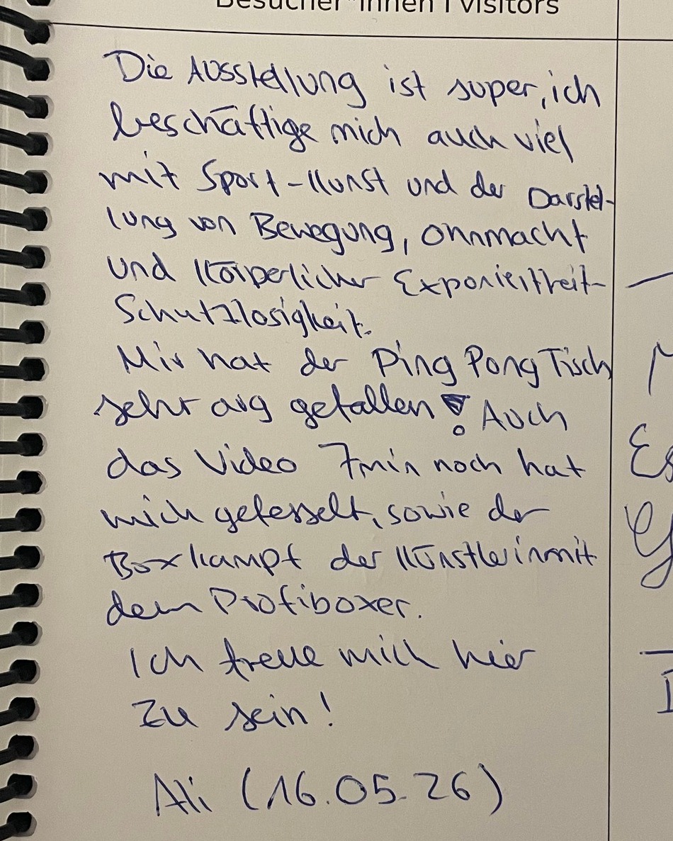 Handgeschriebener Eintrag im Besucherbuch: Lob für die Ausstellung mit Sport-Kunst, Bewegungsdarstellung und dem Ping-Pong-Tisch; erwähnt werden auch ein Video und ein Boxkampf mit Profiboxer. Unterschrieben mit „Ali (16.05.26)“. (KI-Alternativtext)