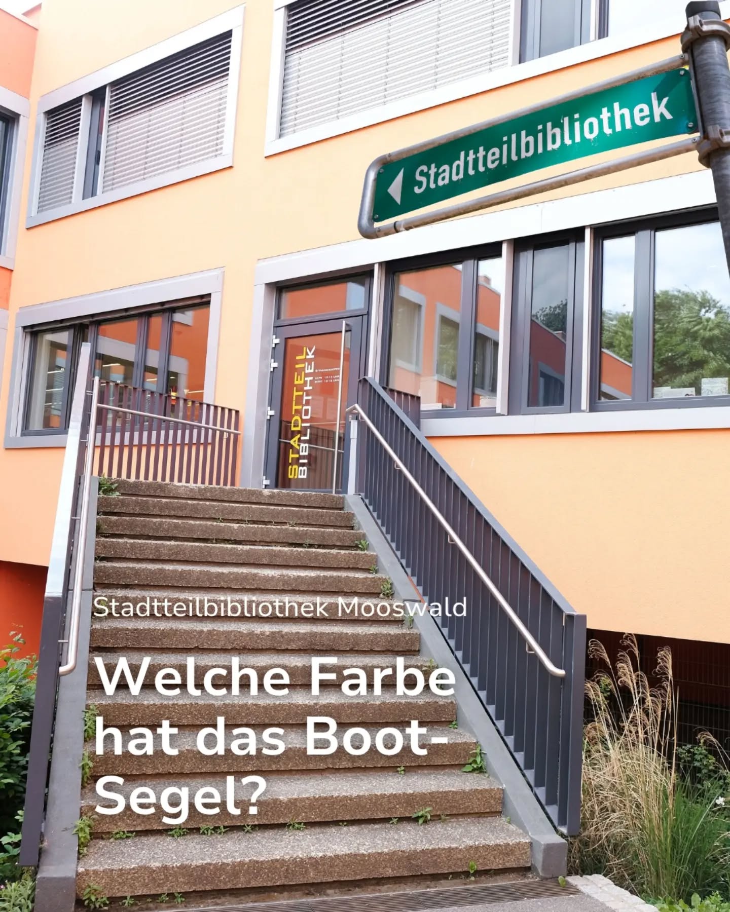 Ein orangefarbenes Gebäude mit einer Treppe zur Eingangstür, auf der vertikal "STADTTEIL BIBLIOTHEK" steht. Ein grünes Straßenschild oben rechts zeigt nach links und trägt die Aufschrift "Stadtteilbibliothek". Auf den Treppenstufen ist weißer Text eingeblendet: "Stadtteilbibliothek Mooswald" und die Frage "Welche Farbe hat das Boot-Segel?". (KI-Alternativtext)