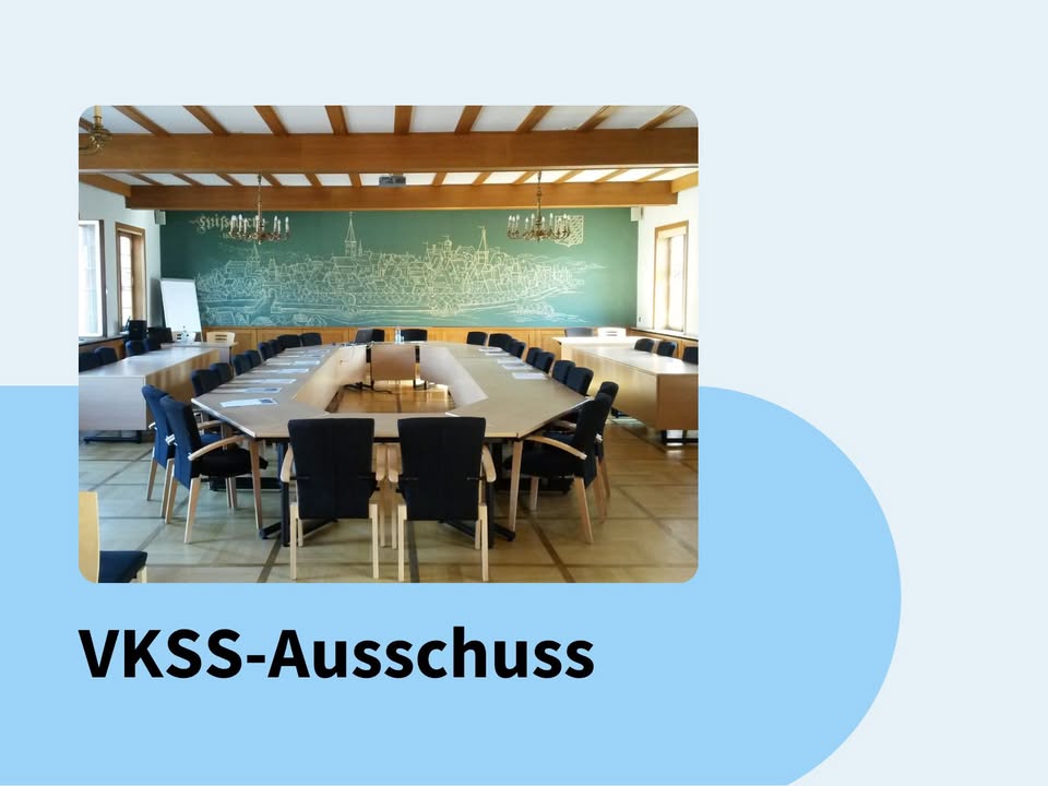 Dieser Alternativtext wurde KI-generiert: Ein Innenraum mit einem großen Konferenztisch und Stühlen. An der Wand befindet sich eine große Darstellung einer Stadtlandschaft vor einer grünen Wand.