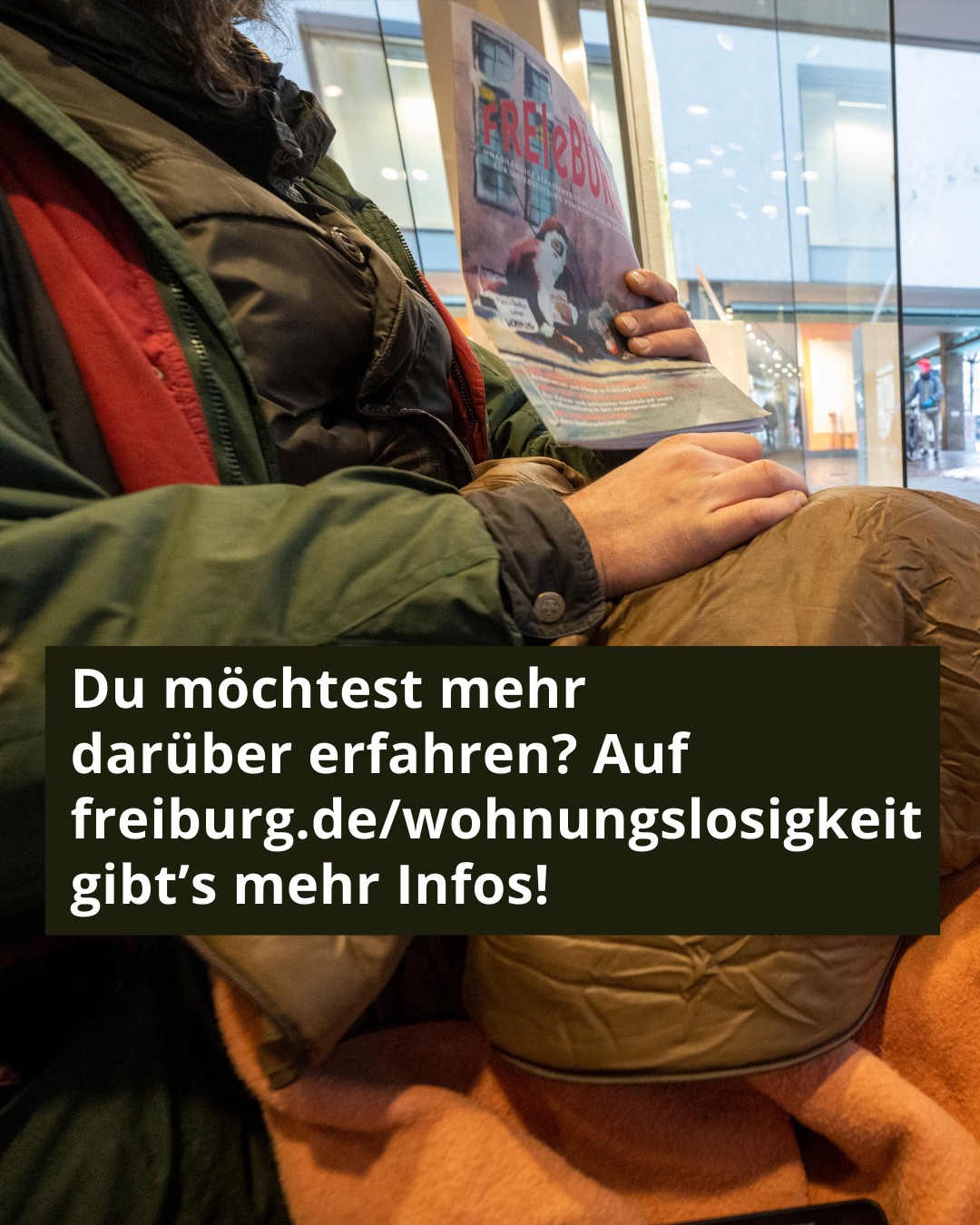 Dieser Alternativtext wurde KI-generiert: Eine Person sitzt und liest eine Broschüre. Die Broschüre enthält Informationen zum Thema Wohnungsnot in Freiburg und verweist auf eine Webseite.