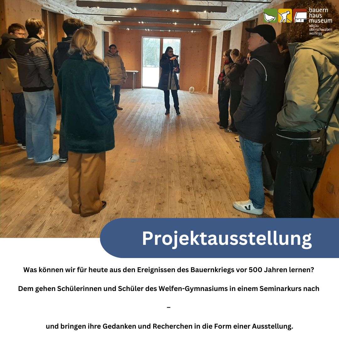 Dieser Alternativtext wurde KI-generiert: Ein Innenraum mit einer Gruppe von Personen, die vor einer geöffneten Tür und einem großen Banner stehen. Das Banner kündigt eine Ausstellung zum Thema Bauernkrieg an.