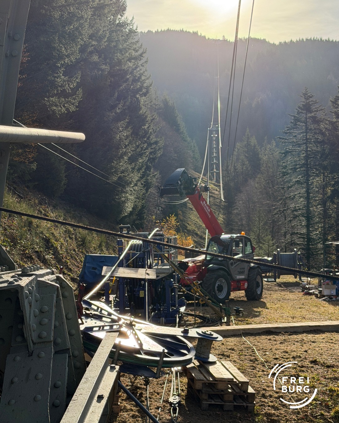 Dieser Alternativtext wurde KI-generiert: Eine Aufnahme zeigt eine Baustelle in einer Waldlandschaft. Im Vordergrund sind Metallstrukturen und schwere Maschinen zu erkennen.