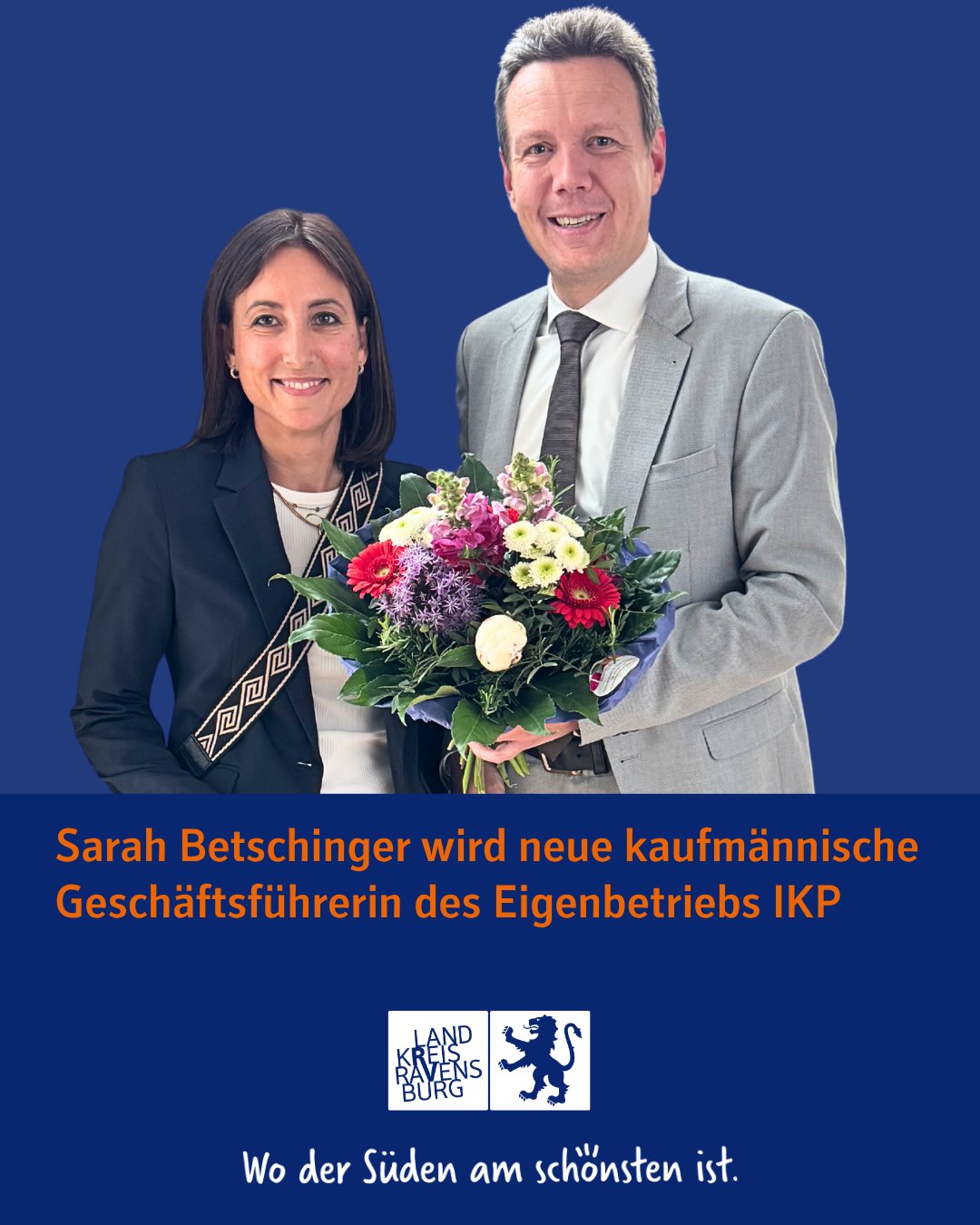 Ein lächelnde Person bekommt einen Blumenstrauß von einer weiteren lächelnden Person. Beide sind formell gekleidet vor einem blauen Hintergrund.