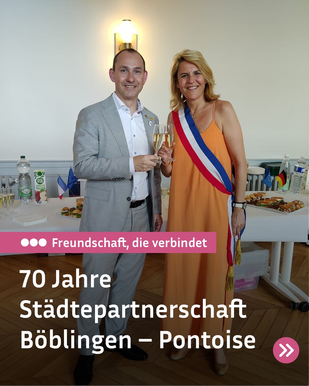 Zwei Personen stehen nebeneinander und halten Champagnergläser, wobei die rechte Person eine blau-weiß-rote Schärpe über einem orangefarbenen Kleid trägt. Im Hintergrund steht ein Tisch mit Speisen und kleinen Flaggen. Ein Text im Vordergrund lautet: „Freundschaft, die verbindet“ und „70 Jahre Städtepartnerschaft Böblingen – Pontoise“. (KI-Alternativtext)