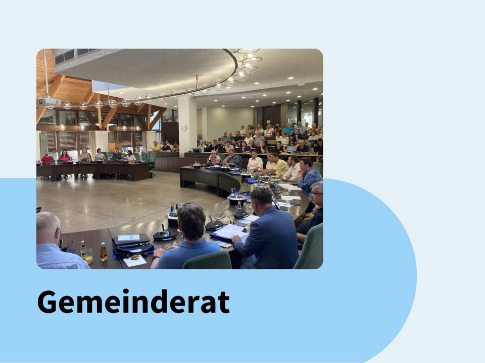 Dieser Alternativtext wurde KI-generiert: Eine Aufnahme zeigt eine Gruppe von Personen, die an einem langen Tisch in einem Raum mit Holzdecken und heller Beleuchtung sitzen. Im Vordergrund sind einige Personen mit Geräten und Dokumenten zu sehen.