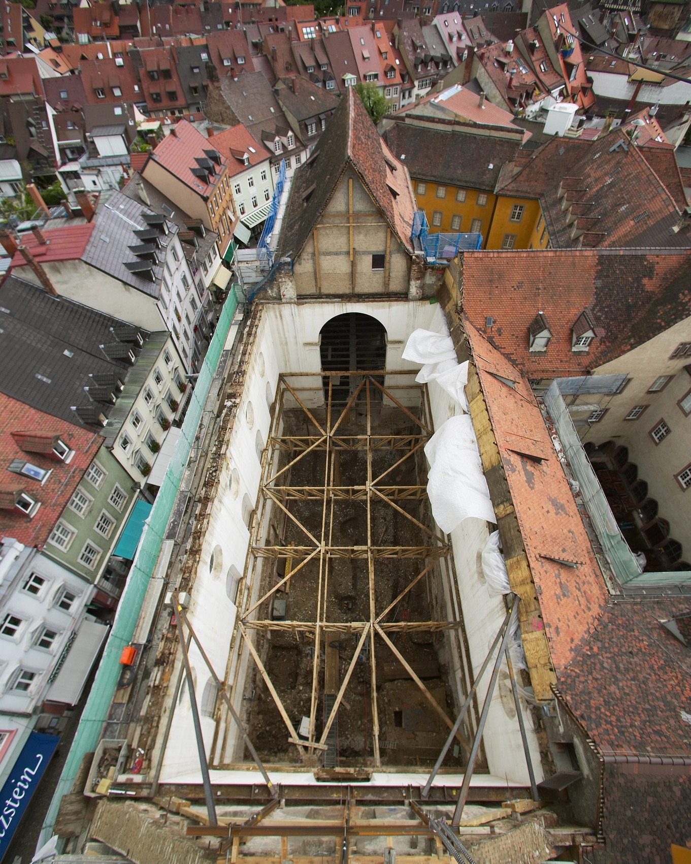 Dieser Alternativtext wurde KI-generiert: Eine Luftaufnahme zeigt Gebäude mit roten Ziegeldächern. Im Vordergrund befindet sich ein Baugerüst um eine unfertige Struktur.
