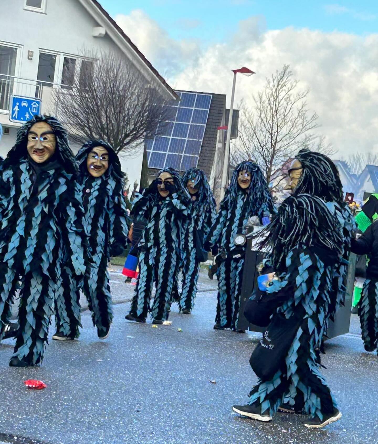 Dieser Alternativtext wurde KI-generiert: Eine Gruppe von Figuren in dunklen, behaarten Kostümen steht auf einer Straße. Im Hintergrund sind Gebäude und Bäume zu sehen.