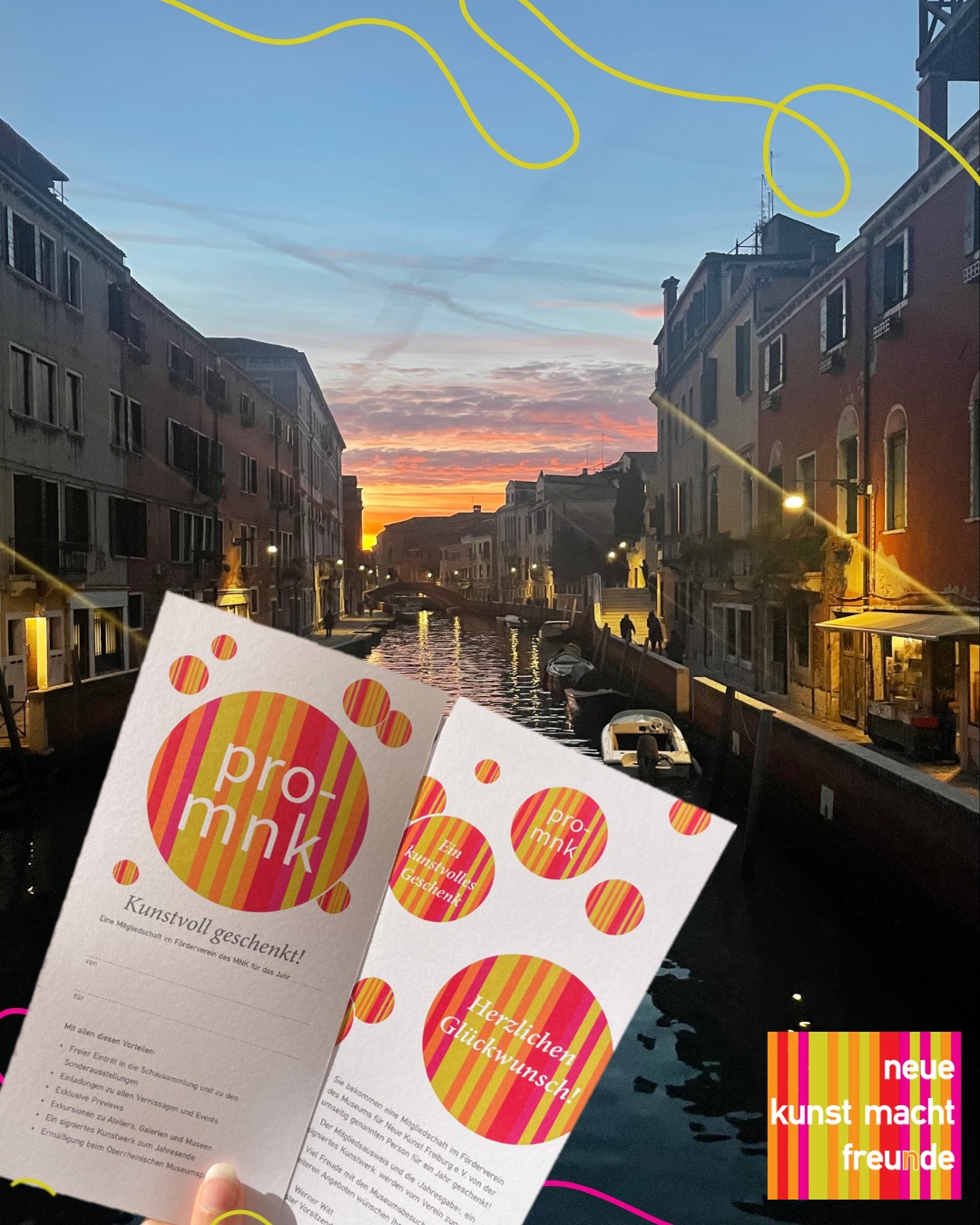 Zwei weiße Karten mit bunten Kreisen und dem Logo „pro-mnk“ werden vor einem Kanal bei Sonnenuntergang gehalten. Die Karten tragen die Texte „Kunstvoll geschenkt!“ und „Herzlichen Glückwunsch!“. Rechts unten ist das Logo „neue kunst macht freunde“ zu sehen. (KI-Alternativtext)