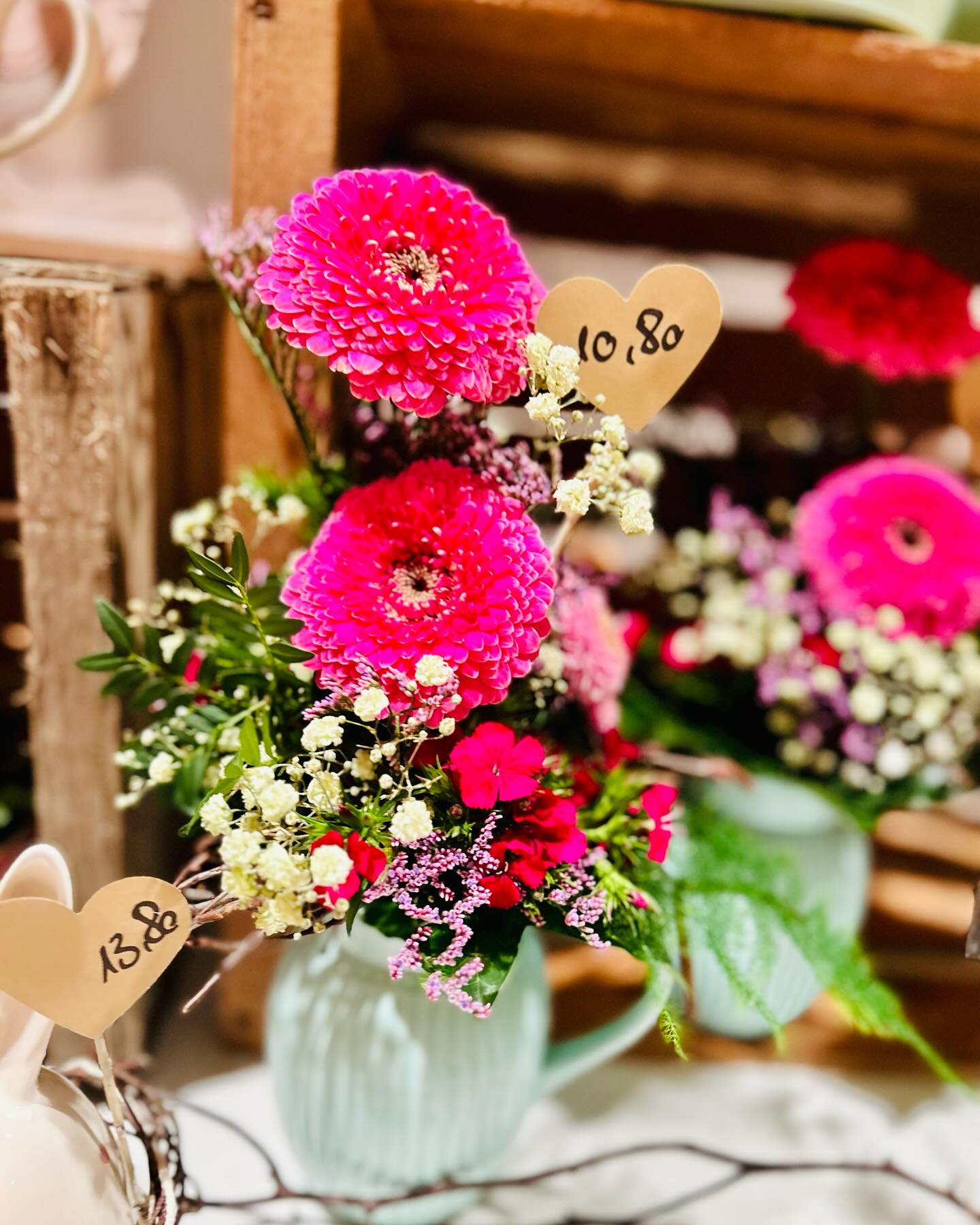 Nahaufnahme von mehreren Blumenarrangements in Vasen vor einem hölzernen Hintergrund. Herzen mit Preisen sind neben den Blumen sichtbar.