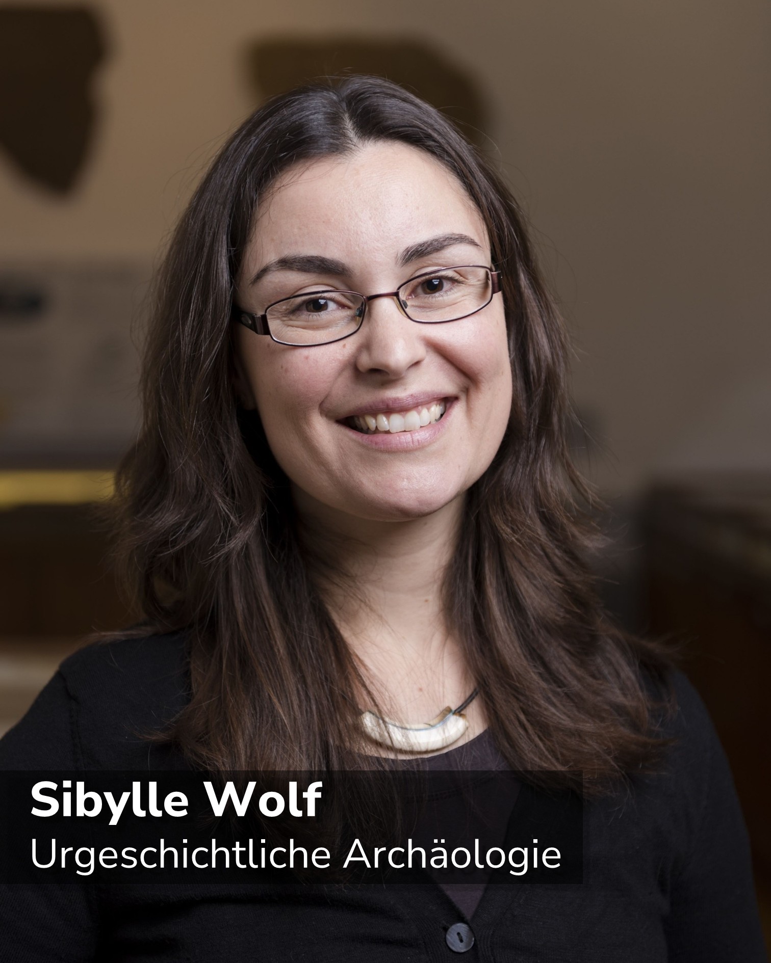 Dieser Alternativtext wurde KI-generiert: Porträt einer lächelnden Person mit Brille. Der Hintergrund ist unscharf und weist warme Farbtöne auf.